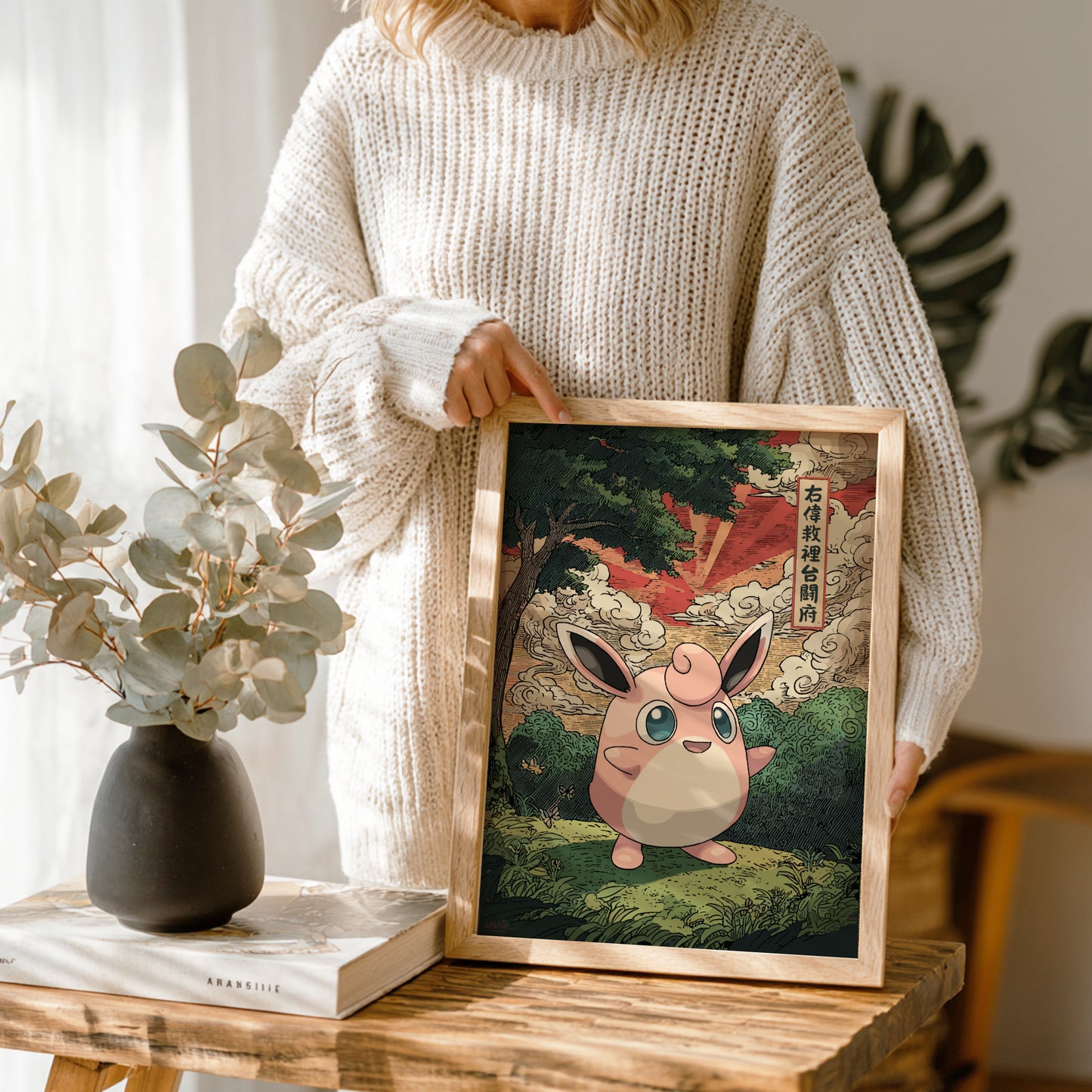 Person holding a framed illustration of Wigglytuff Pokemon character in a natural setting