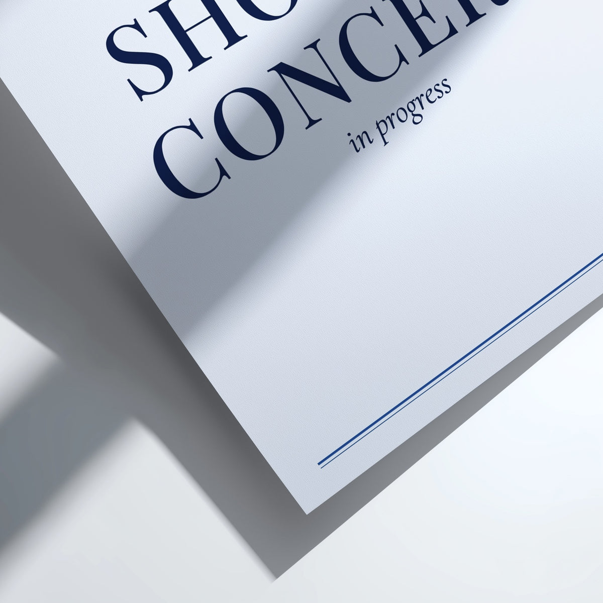 A close-up of a white paper or card with large black text reading 'SHOW' and 'CONCERT' and smaller text 'in progress', plus a thin blue line near the bottom, photographed on a white surface with strong shadows.