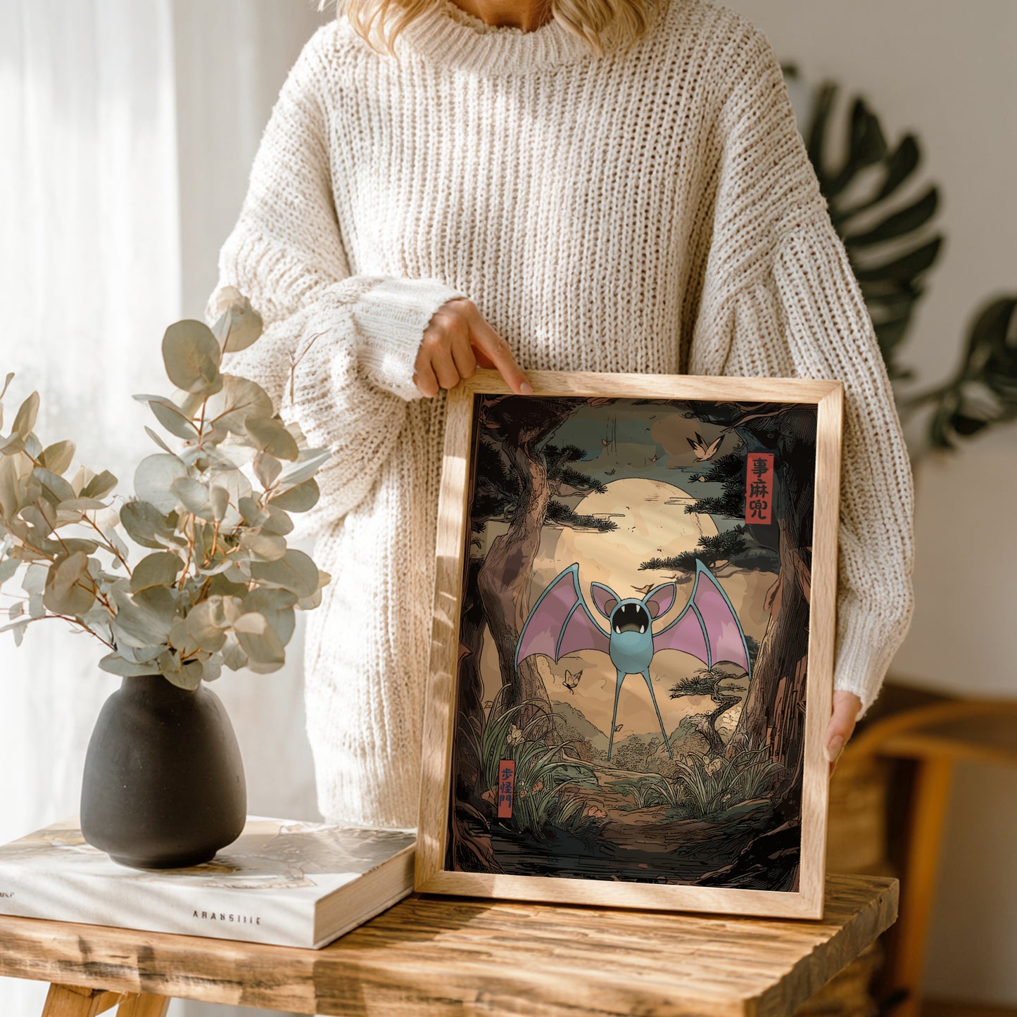 Person holding a framed artwork of Zubat Pokemon in a home setting.