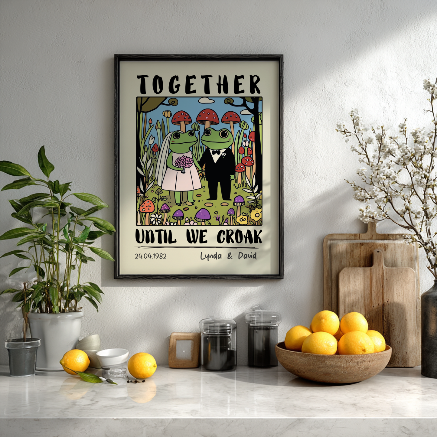 Framed artwork with frogs in wedding attire on a wall above a kitchen counter.