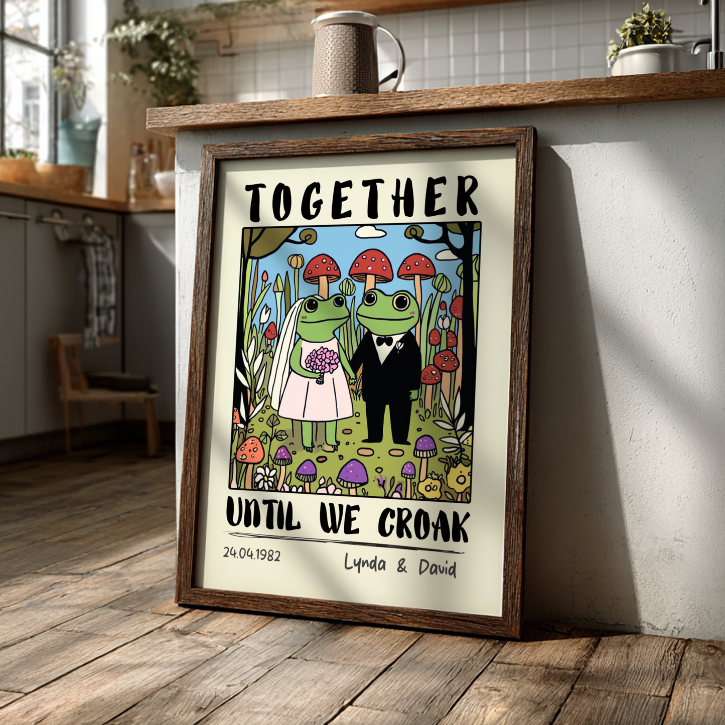 Framed artwork with cartoon frogs in wedding attire and text 'Together until we croak' on a kitchen counter.