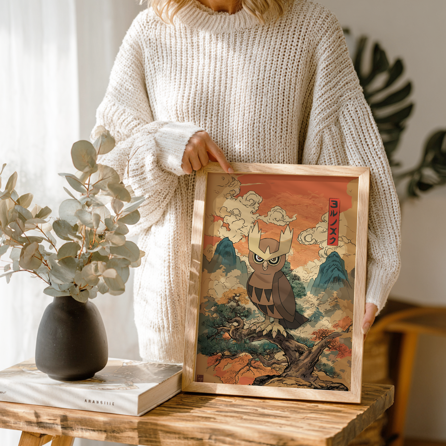 Person holding a framed artwork of Noctowl Pokémon in a natural setting