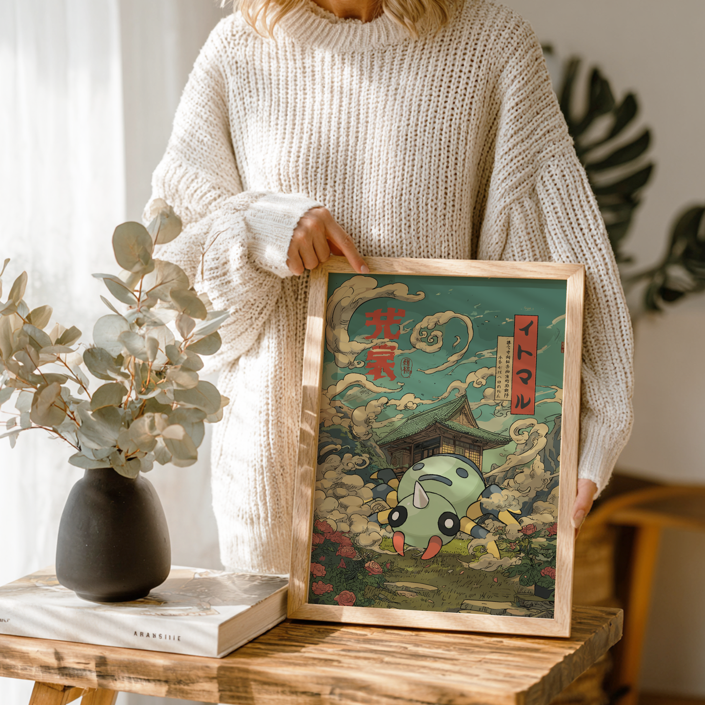 Person holding a framed artwork with Spinarak Pokémon character and traditional Japanese elements on a wooden table.