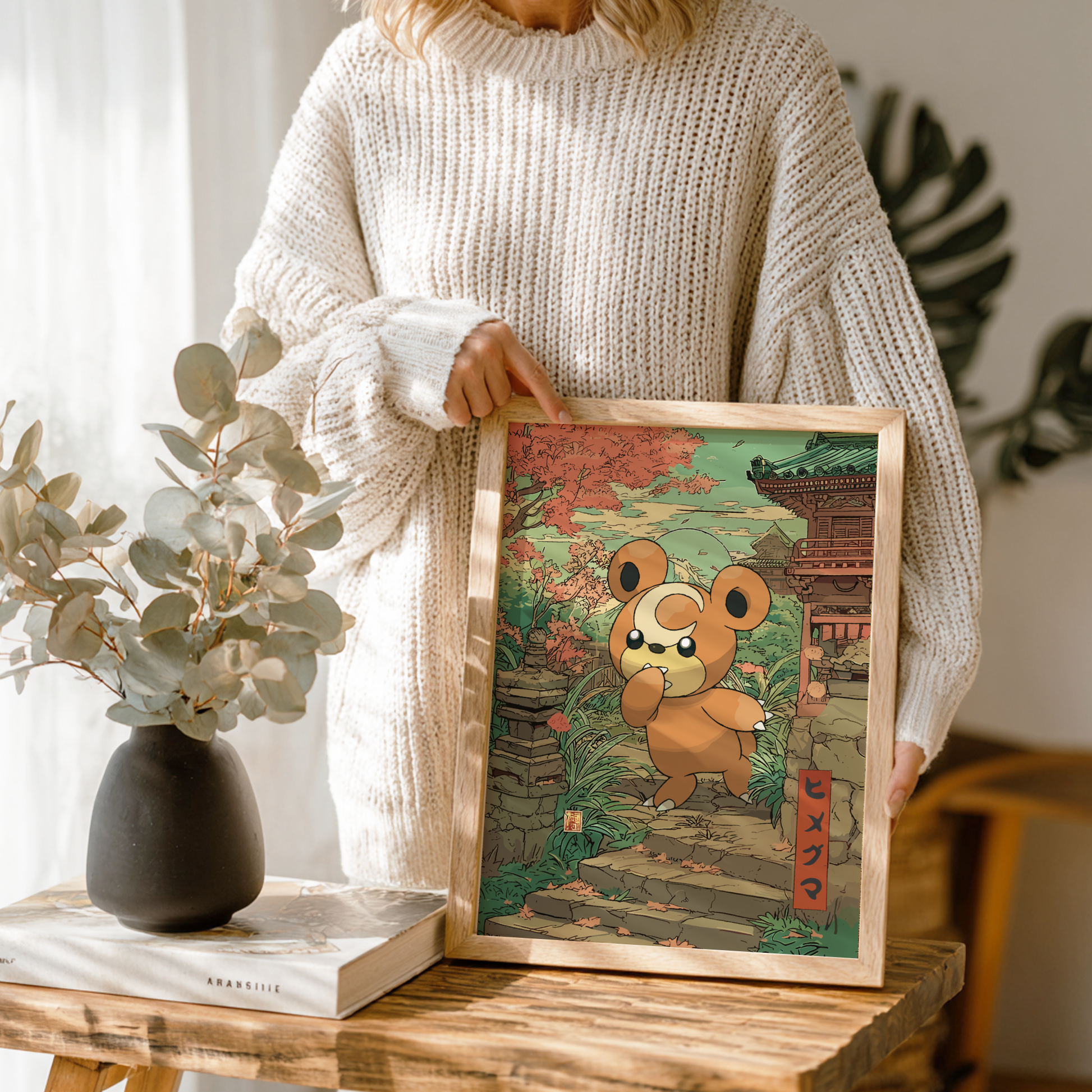 Person holding a framed illustration of Teddiursa Pokemon in a traditional setting on a wooden table.