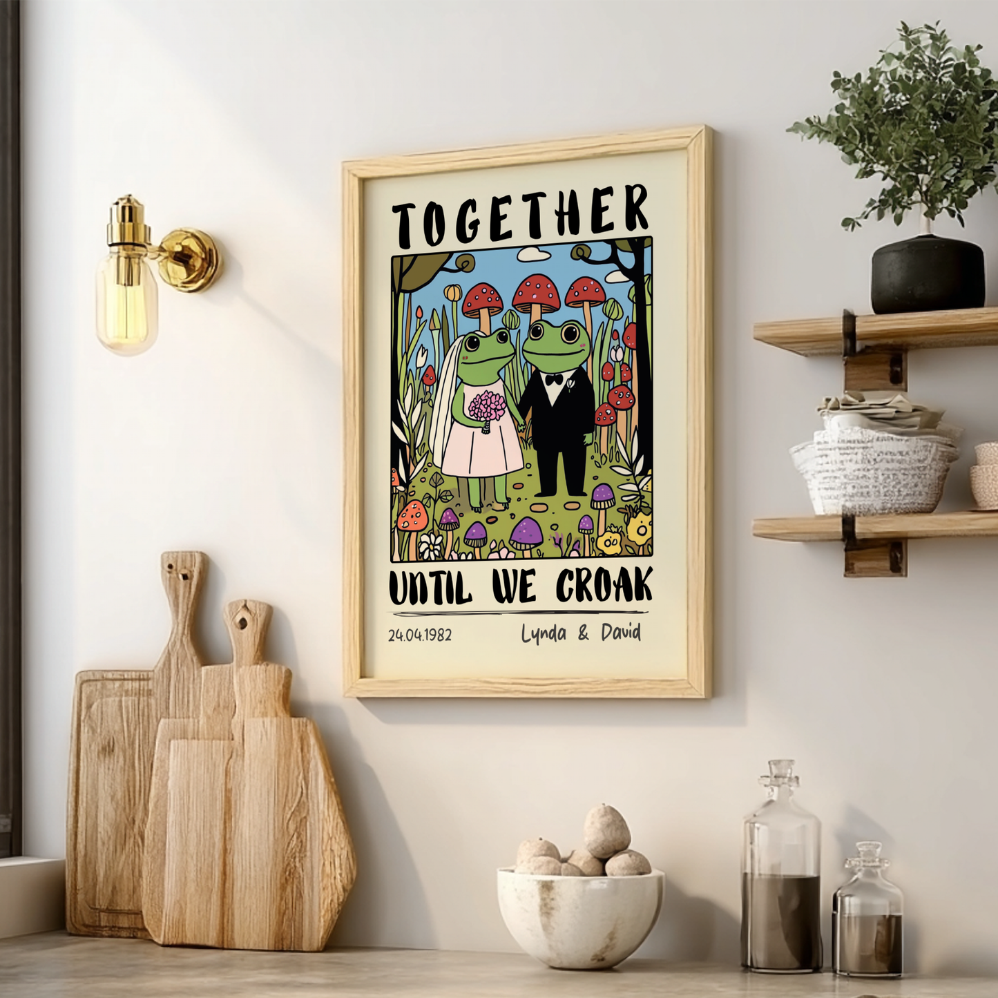 Framed artwork with cartoon frogs and text 'Together Until We Croak' on a wall with decor items below.
