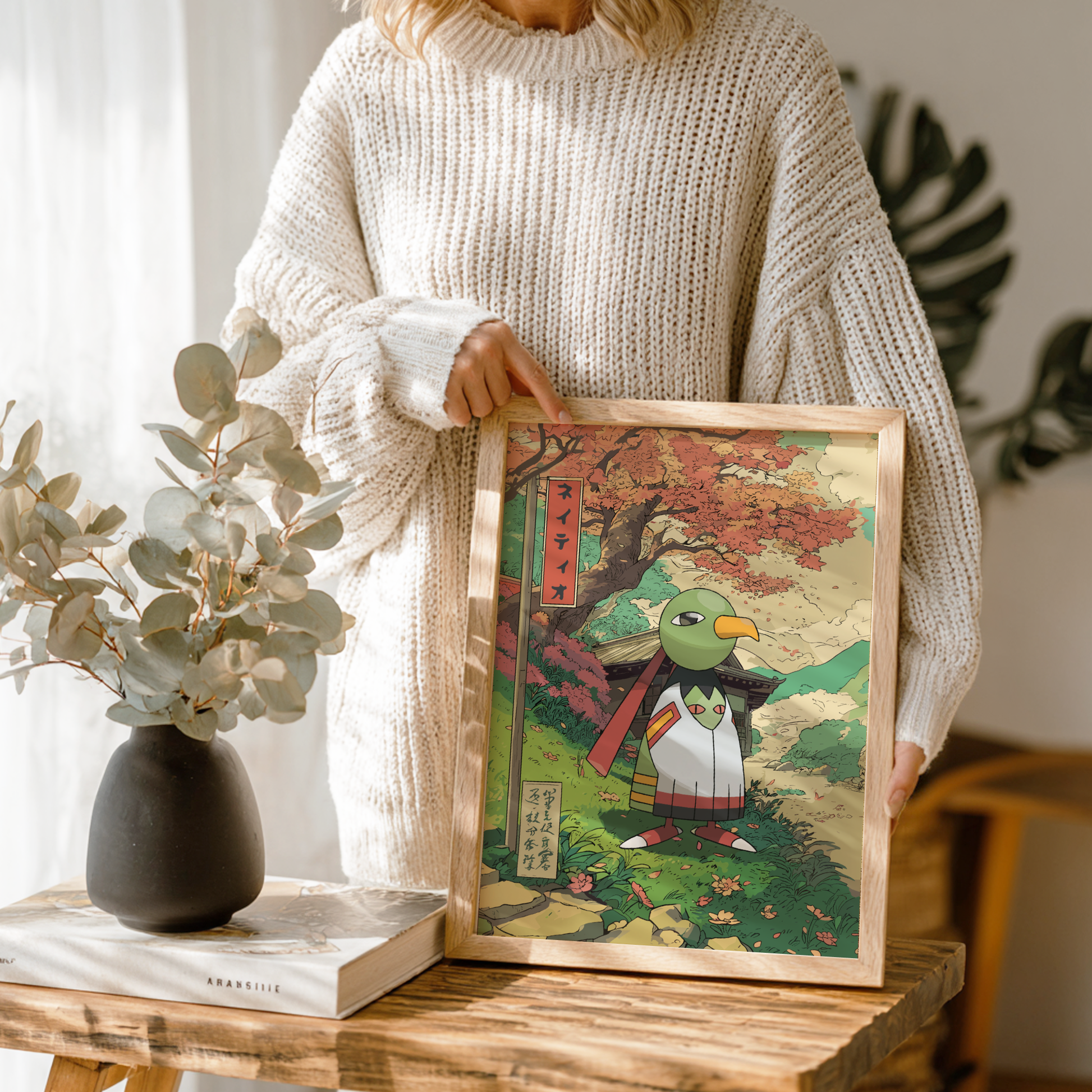 Person holding a framed artwork of Xatu Pokémon on a wooden table.