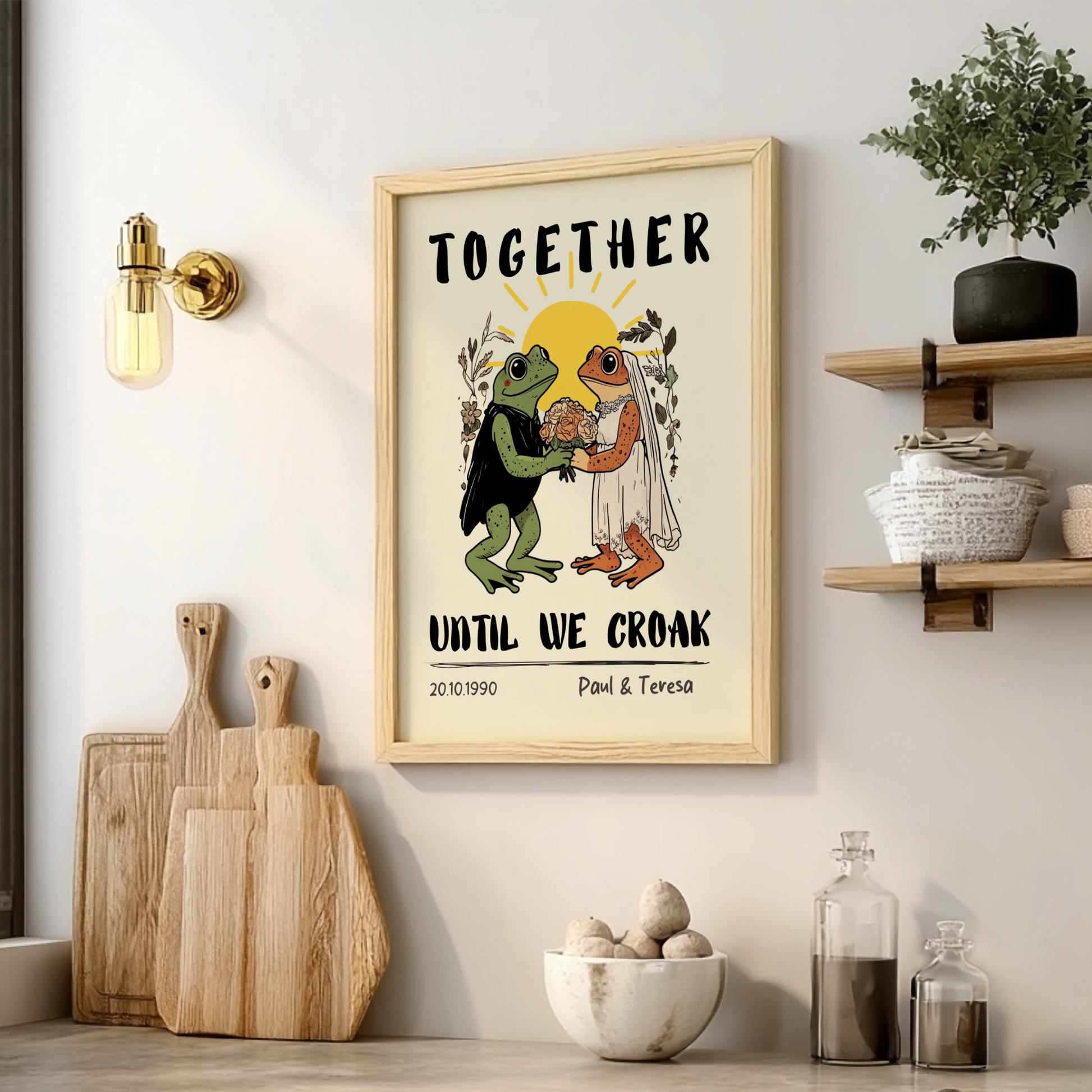 Framed artwork with frogs and text on a wall above a shelf with decor items.