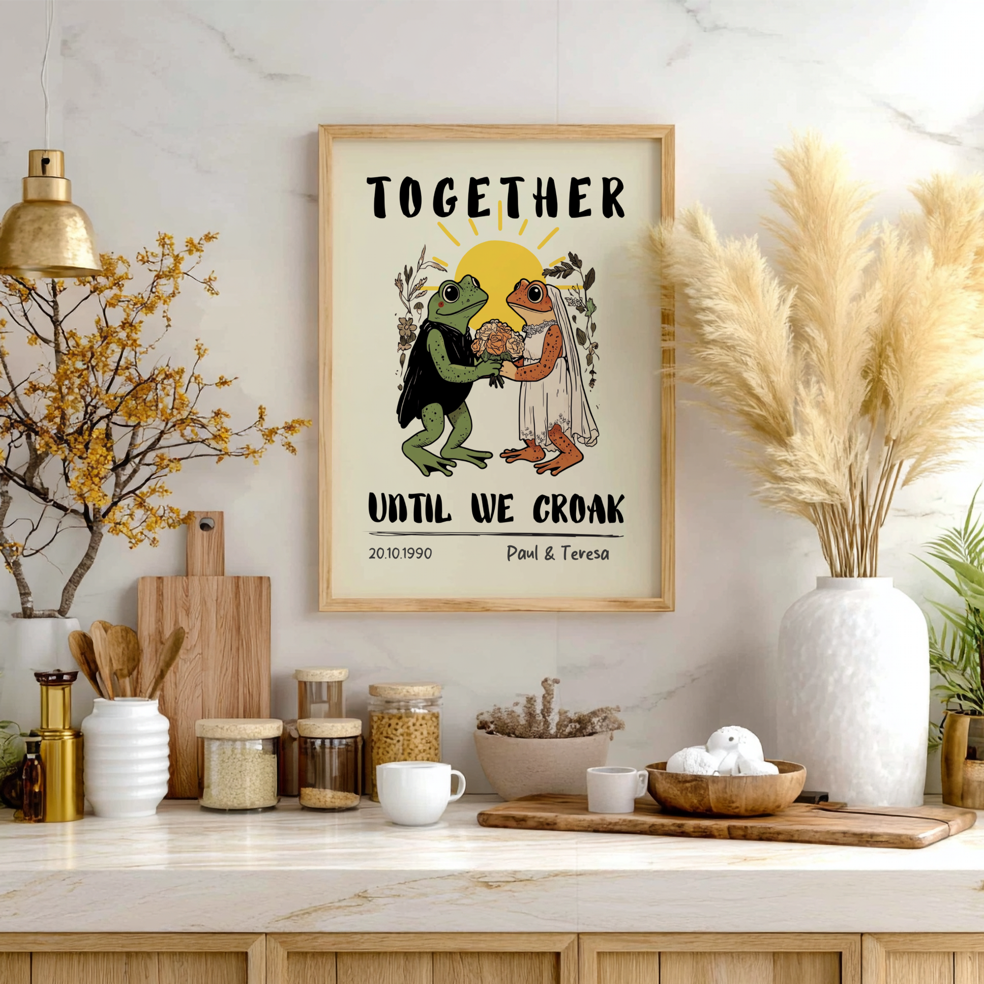 Framed artwork with frogs and text on a kitchen wall with decor items.