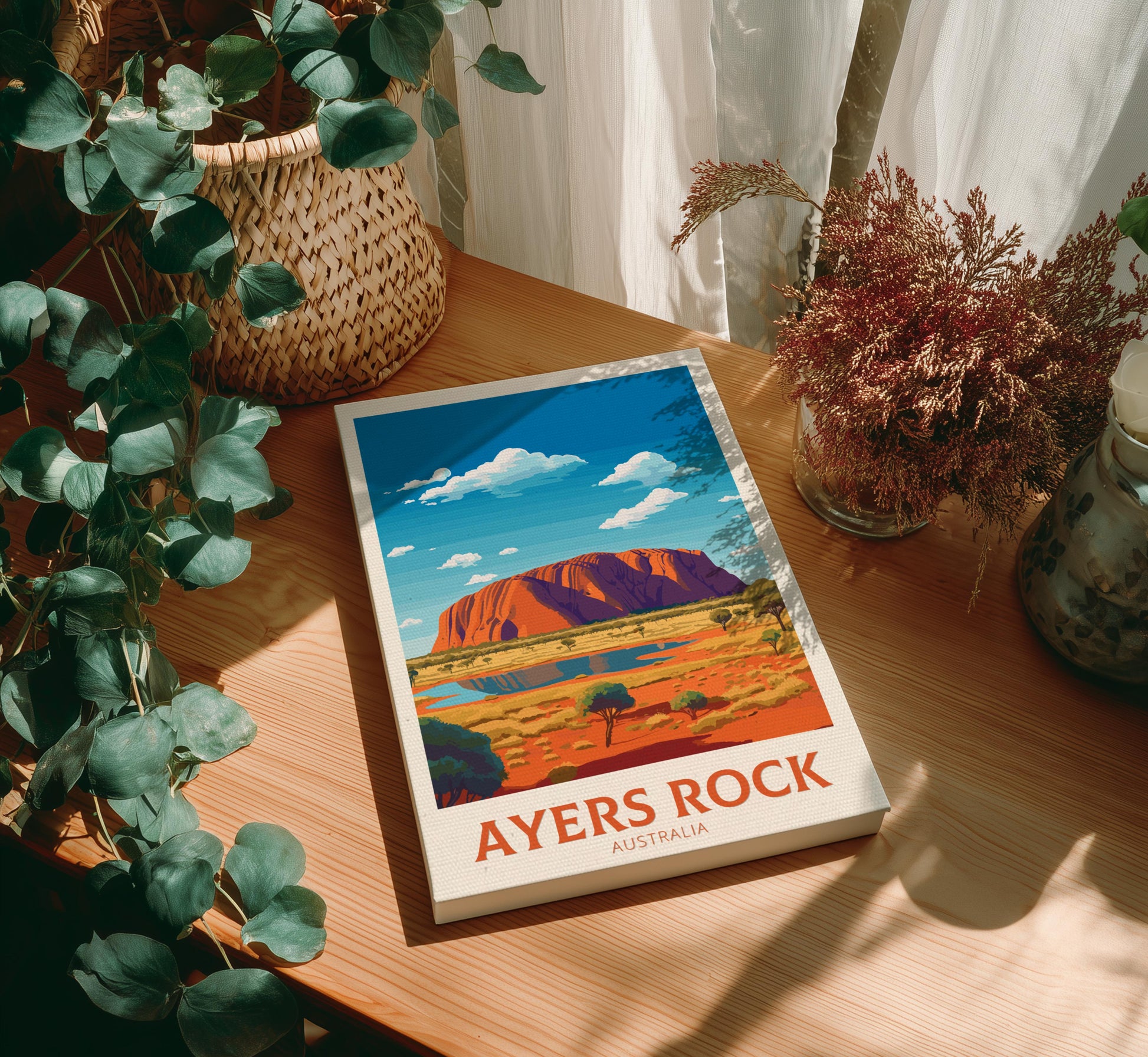 Canvas of 'Ayers Rock, Australia' on a wooden surface with plants around