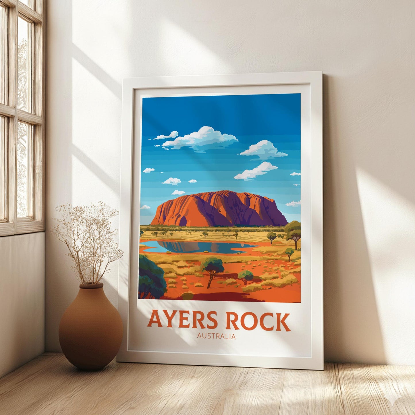 Framed poster of Ayers Rock in a room with a vase on a wooden floor.