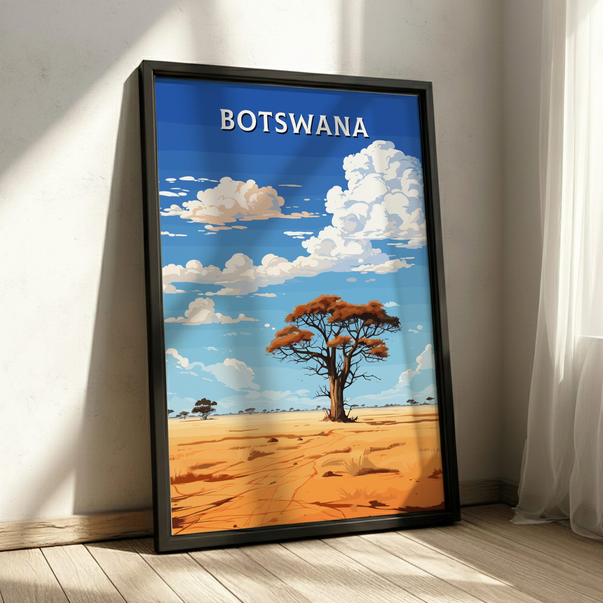 Framed artwork of a desert landscape with a tree and blue sky, labeled 'Botswana', on a wooden floor.