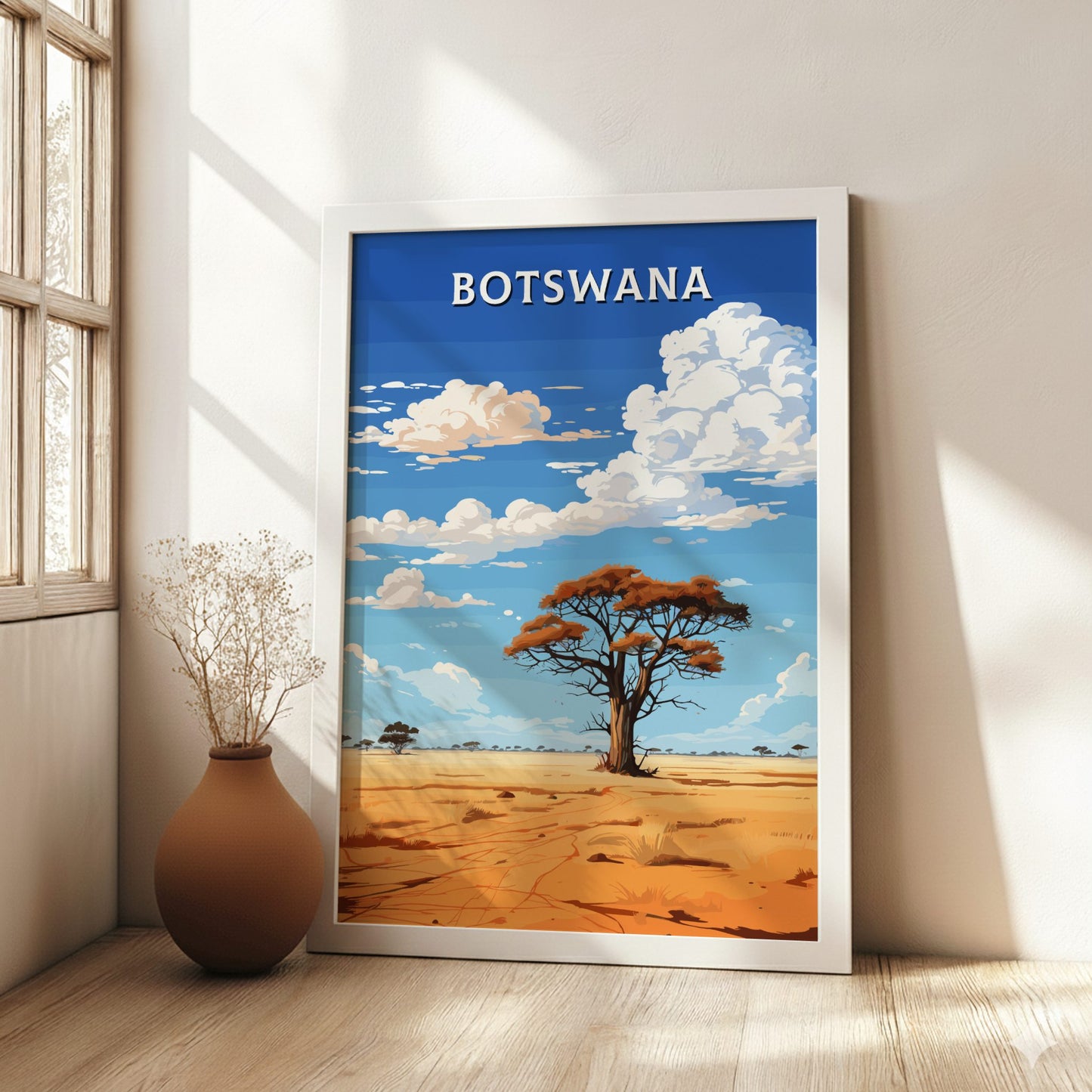 Framed artwork of a desert landscape with a tree and 'BOTSWANA' text, placed on a wooden floor.