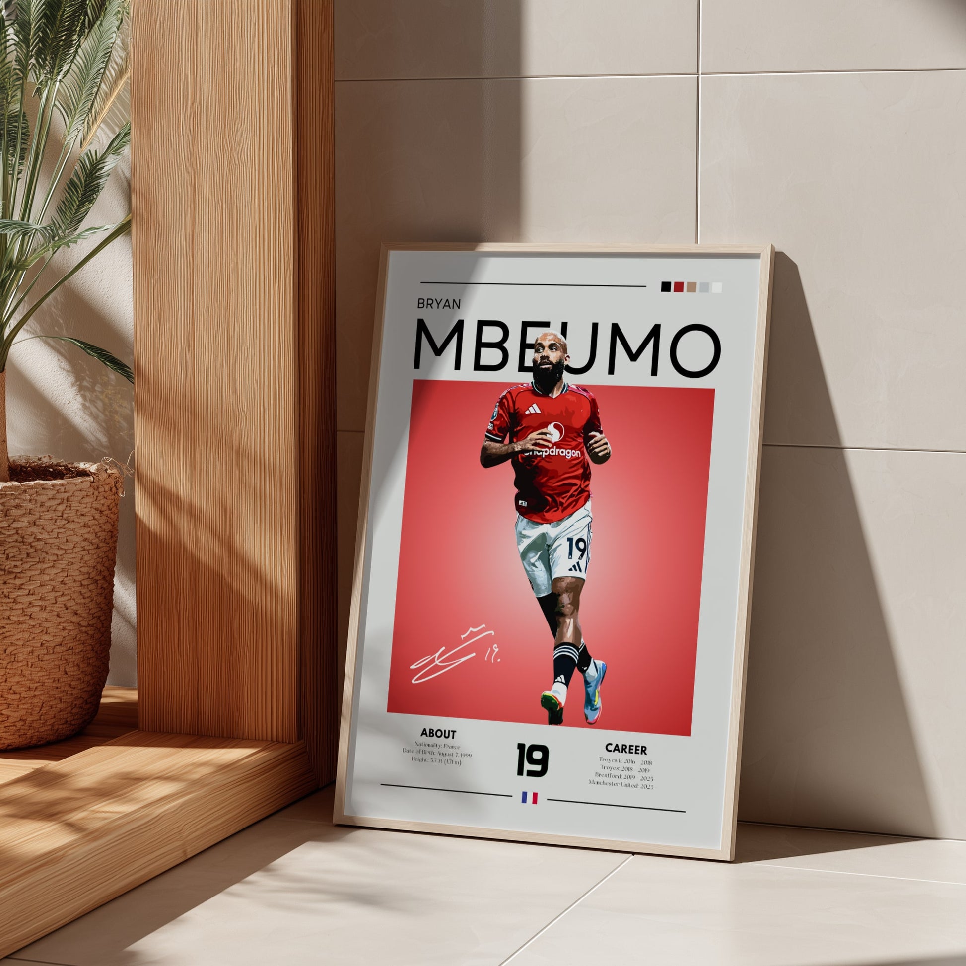 Framed poster of a soccer player with 'Bryan Mbeumo' on a red background, leaning against a wall.