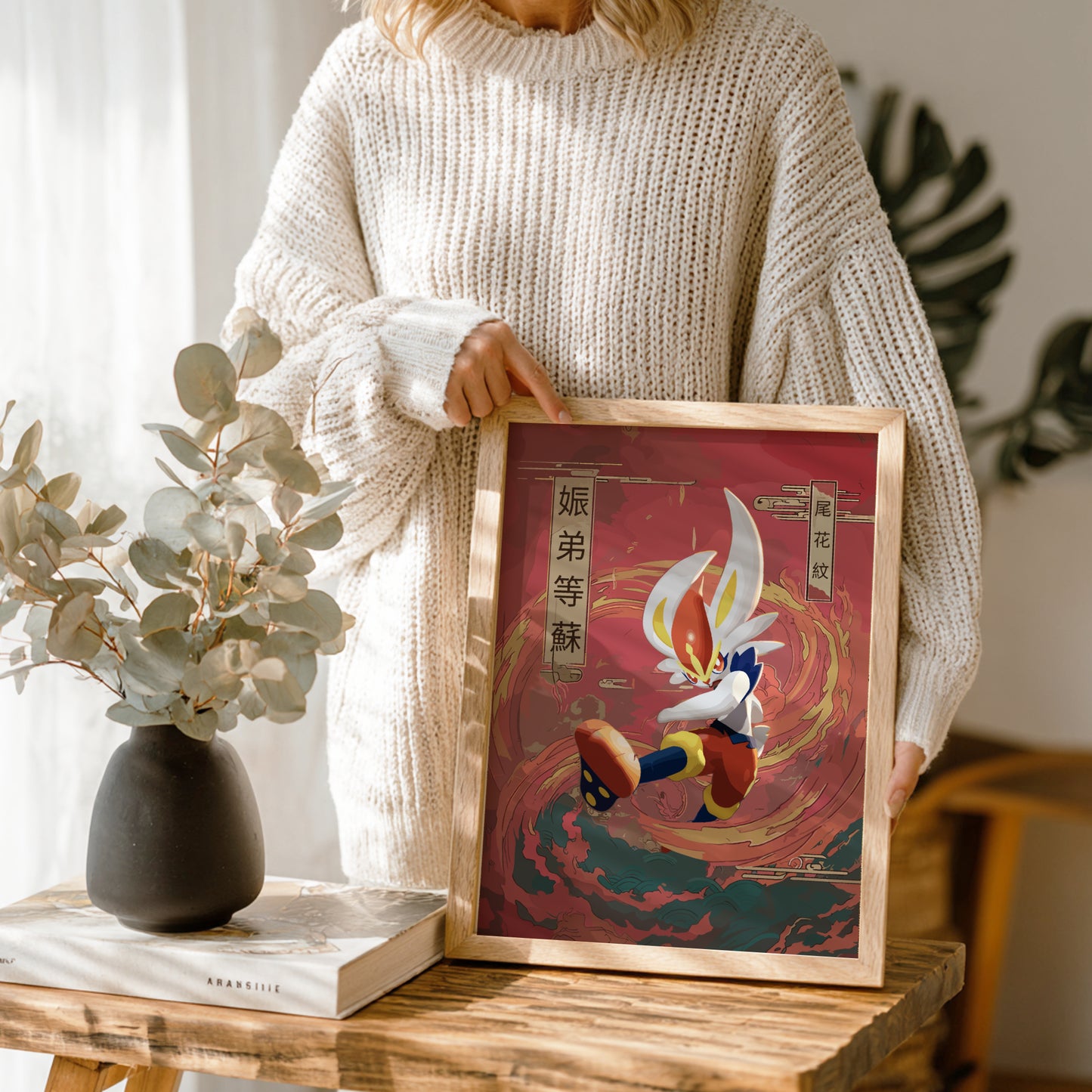 Person holding a framed artwork with a Cinderace Pokemon character design on a wooden table.
