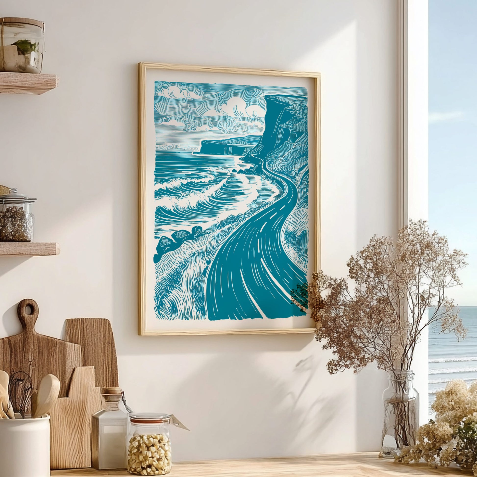 Framed artwork of a coastal scene with a winding road on a wall in a room with wooden shelves and decor.