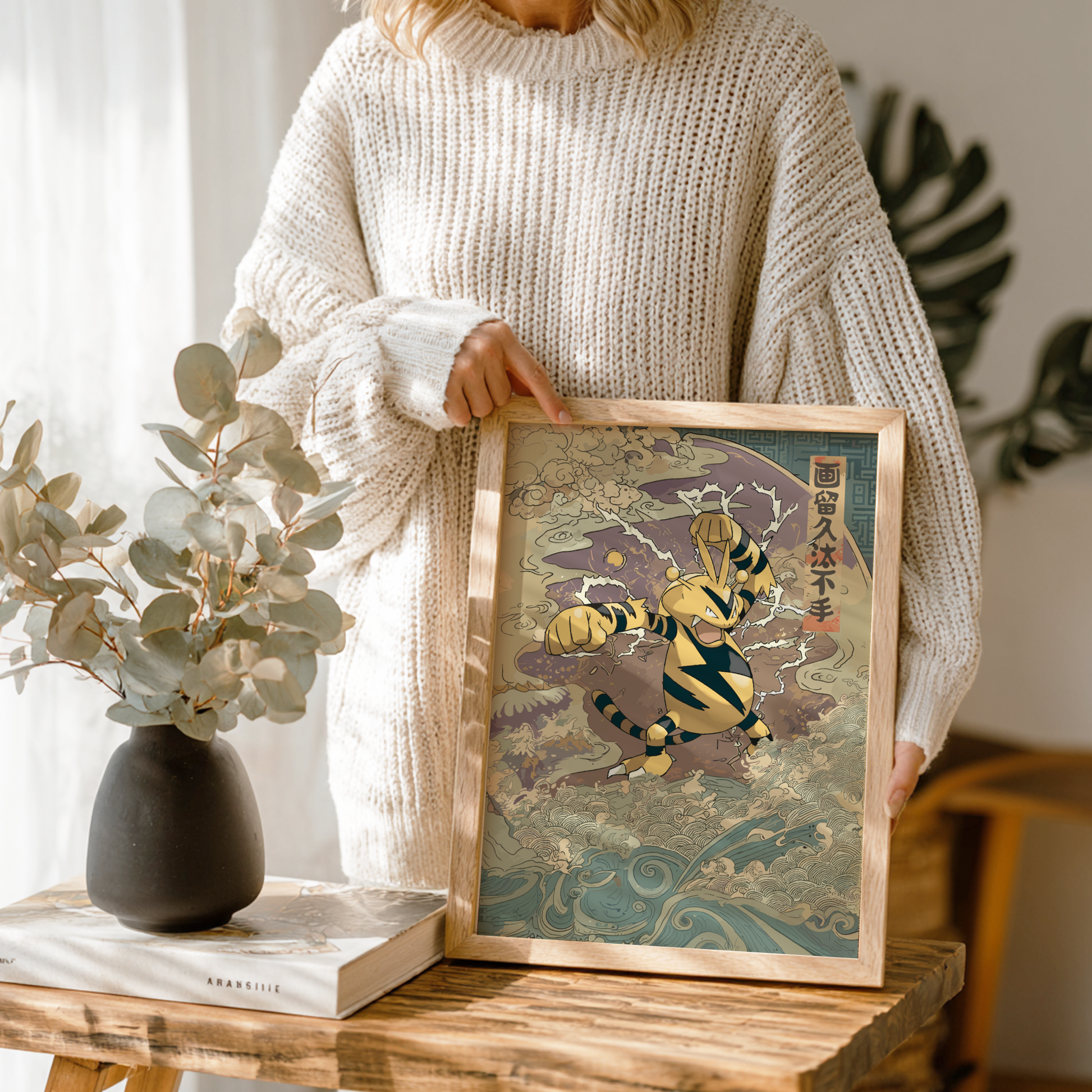 Person holding a framed artwork of Electabuzz Pokemon character with a plant and vase on a table.