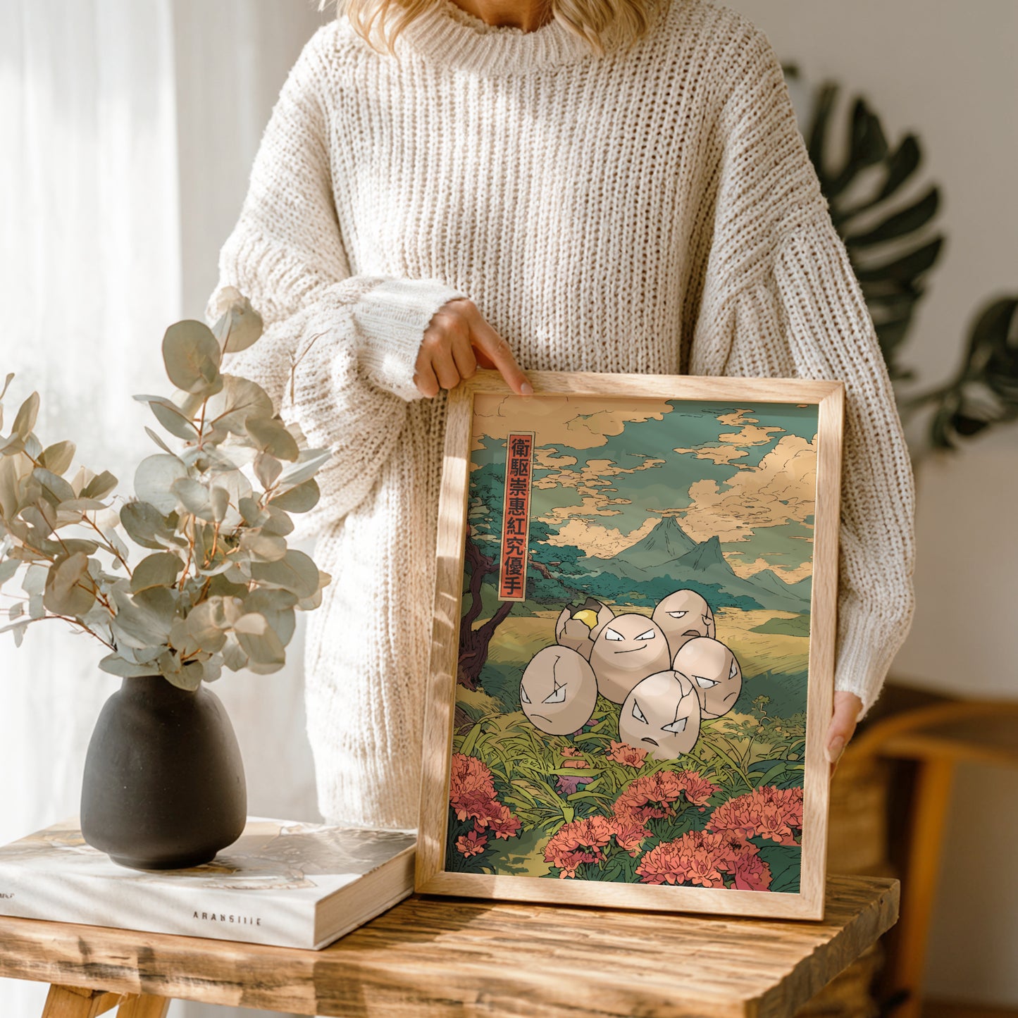 Person holding a framed artwork of Exeggcute Pokemon characters in a room with plants and decor.