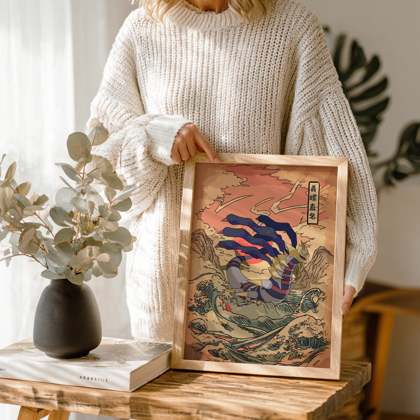 Person holding a framed artwork with Giratina Pokemon design in a home setting