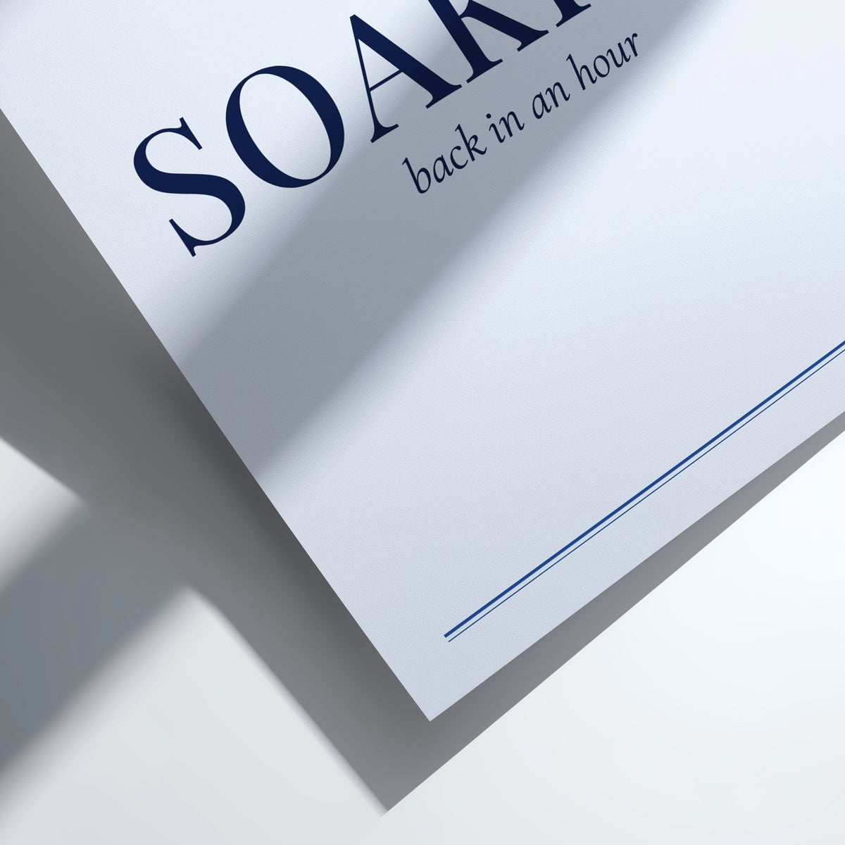 A close-up of a white paper envelope or document with the partial brand name 'SOAKI' in dark navy text and the phrase 'back in an hour' printed below, shown on a white surface with a soft shadow.