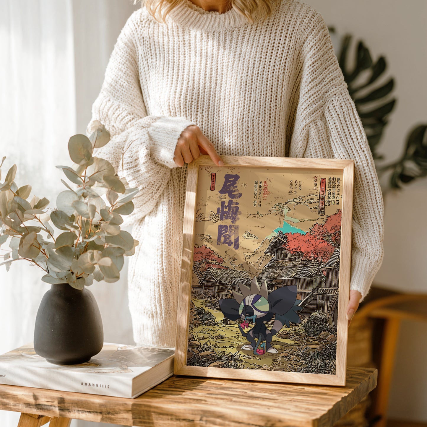 Person holding a framed artwork with traditional Grafaiai Pokemon design on a wooden table.