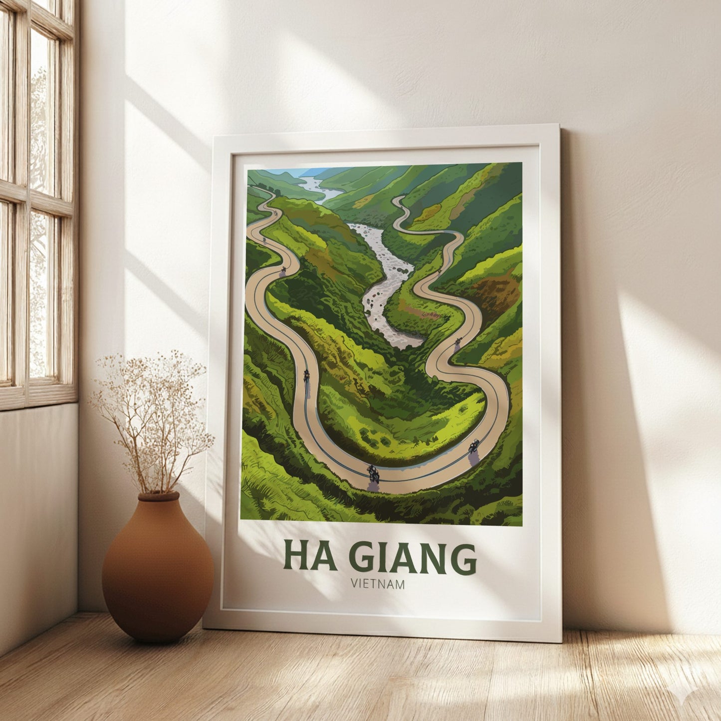 Framed poster of a winding road through green hills with 'Ha Giang Vietnam' text, placed on a wall.