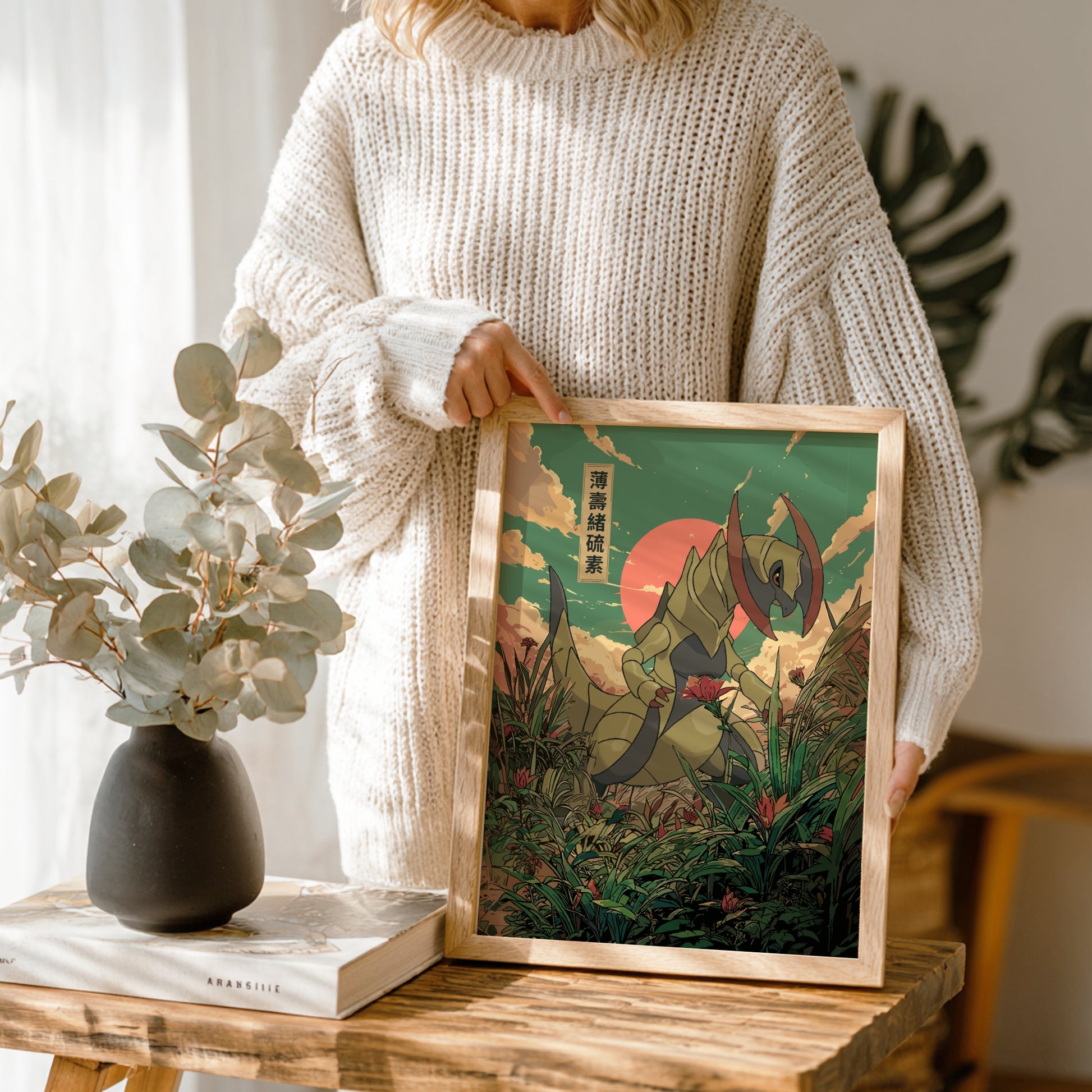 Person holding a framed artwork of Haxorus Pokemon in a forest with a vase and book on a table.