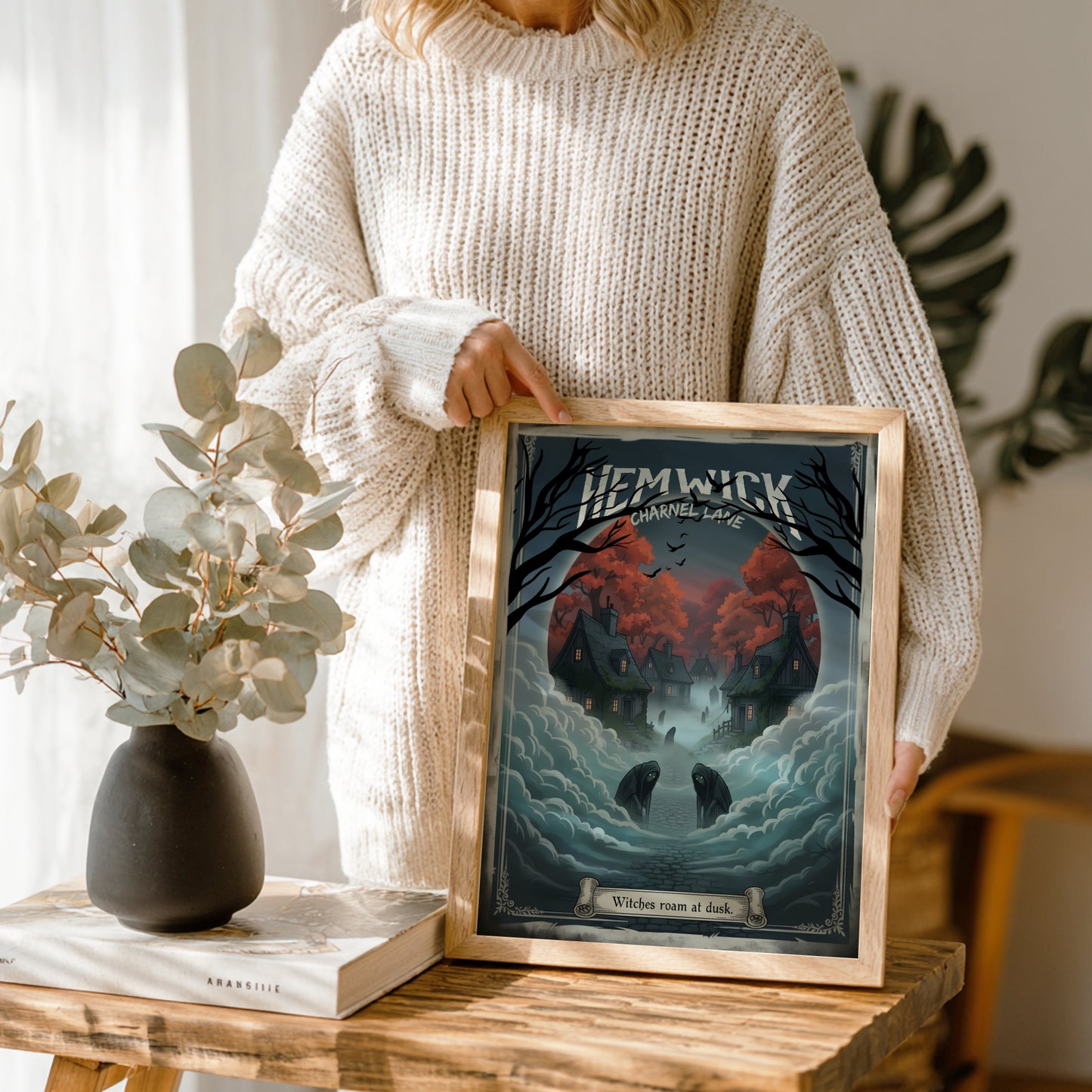 Person holding a framed artwork of Hemwick Charnel Lane from Bloodborne on a wooden table with decor items.