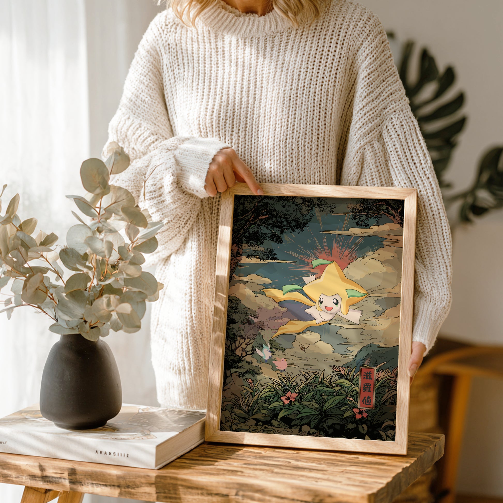 Person holding a framed artwork of Jirachi Pokemon character in a natural setting