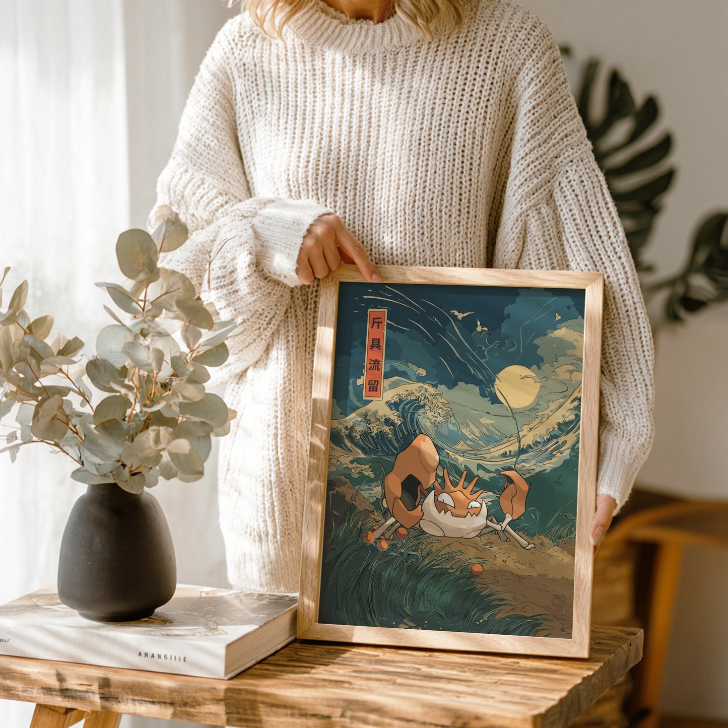Person holding a framed artwork of a traditional Japanese with Kingler Pokemon on a scene with a wave and two figures.