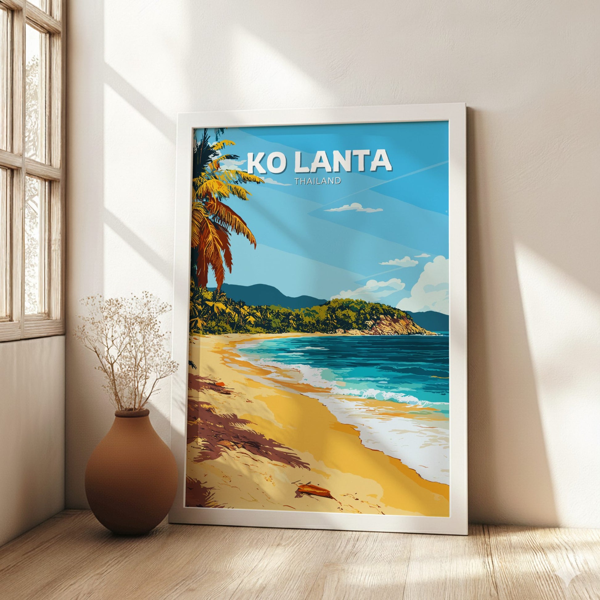 Framed artwork of a tropical beach scene with 'KO LANTA' text, placed on a wooden floor.