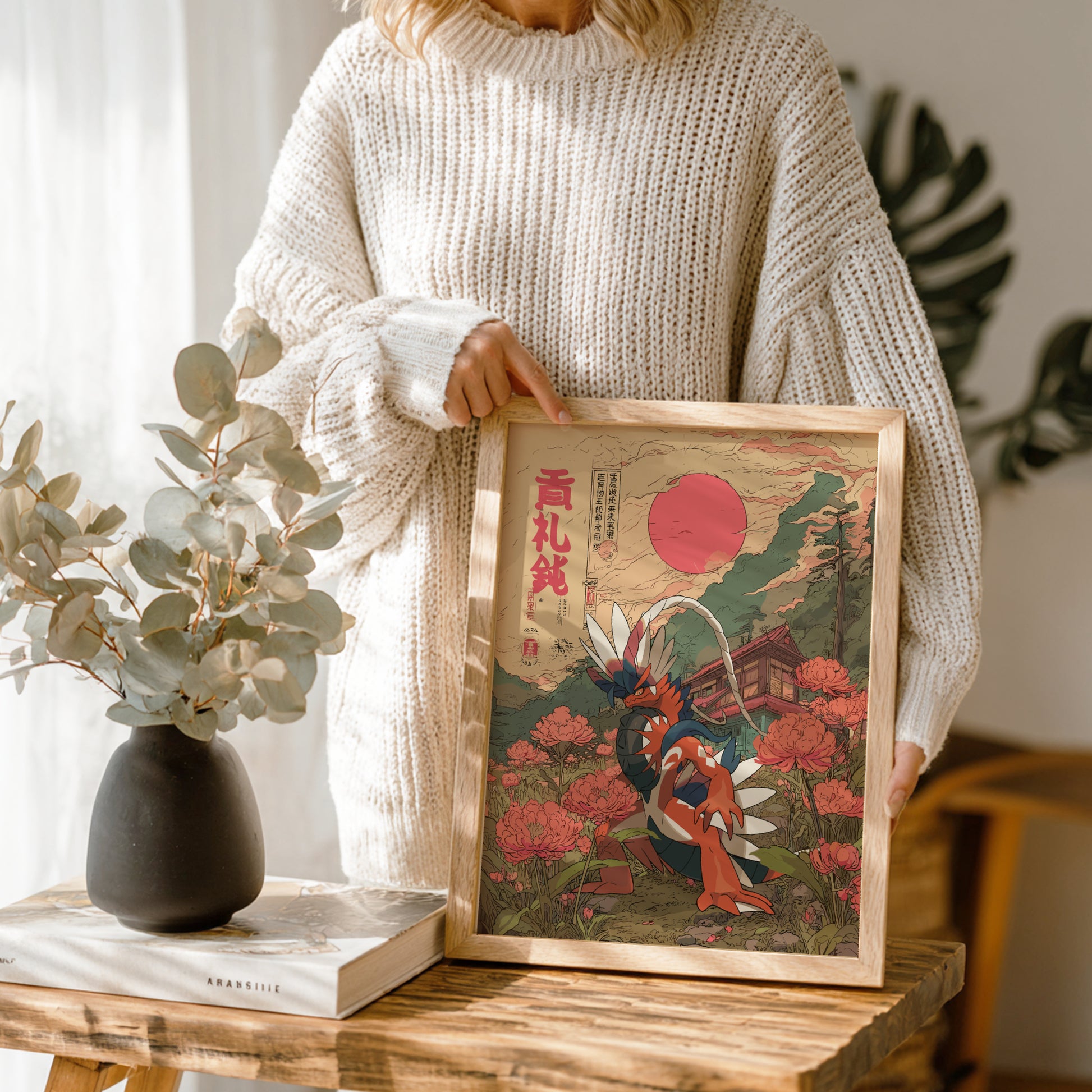 Person holding a framed artwork with Koraidon Pokemon design on a wooden table.