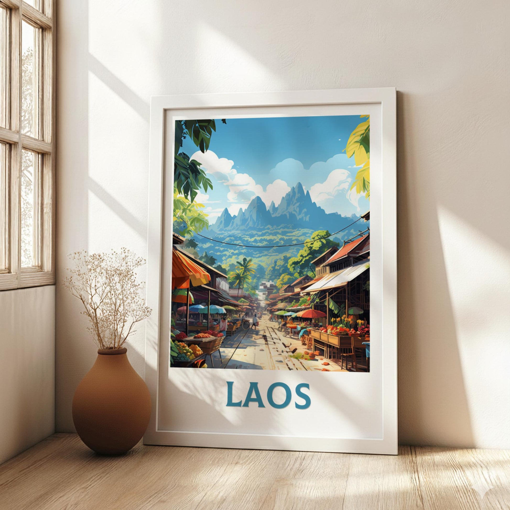 Framed artwork of a Laos street scene with mountains in the background, placed on a wooden floor.