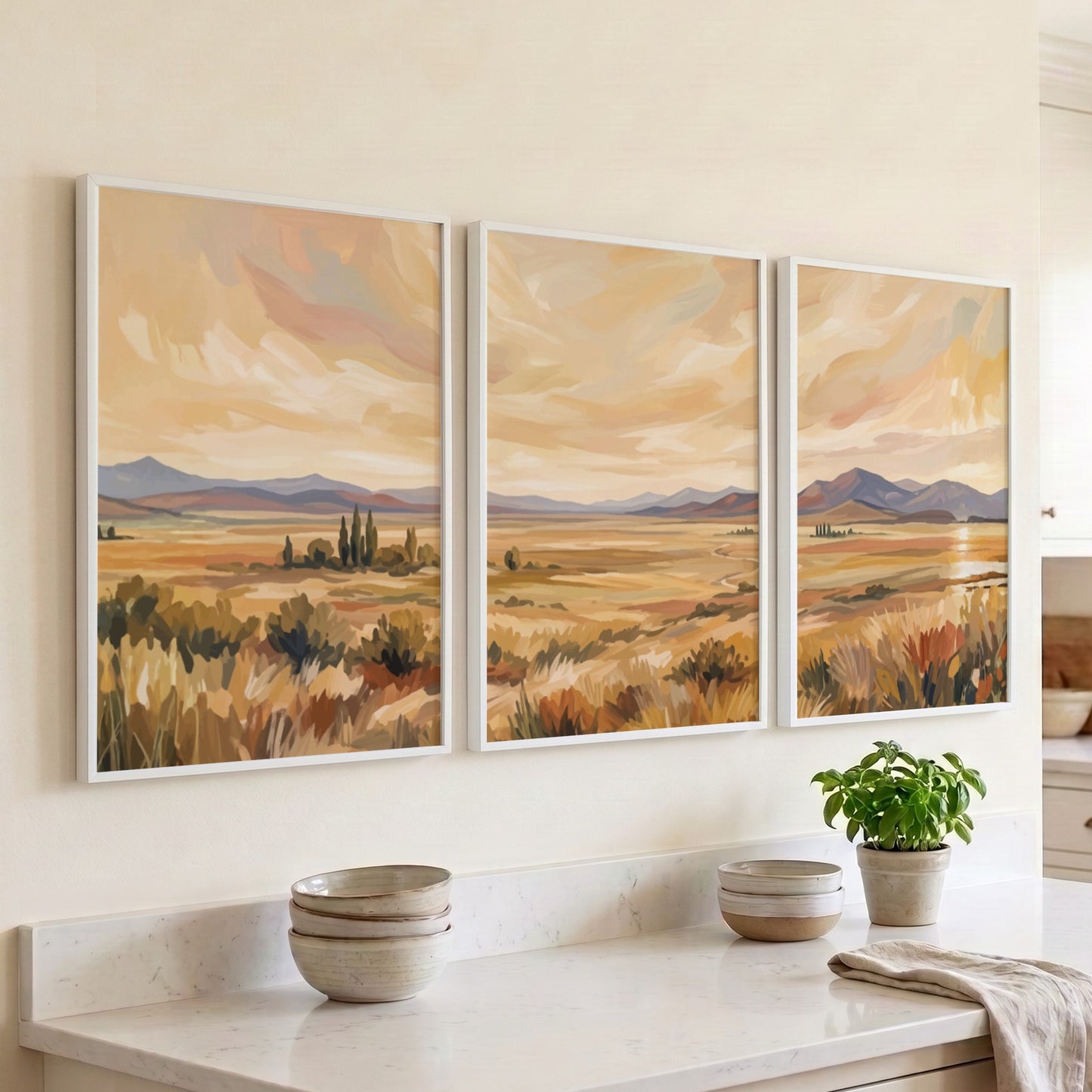 Three framed landscape prints showing golden prairies and distant mountains in a painterly style.