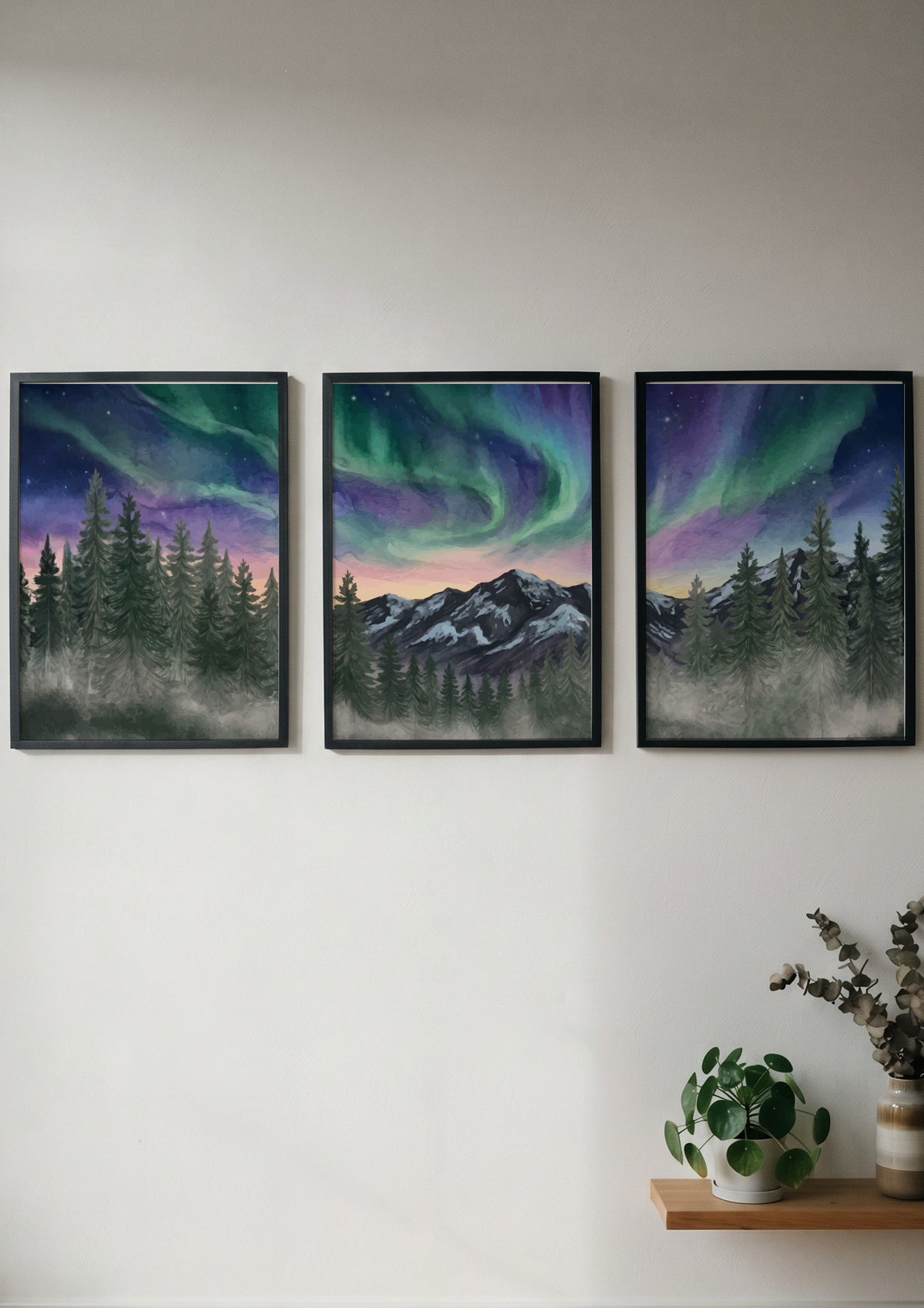 Three framed landscape prints showing green and purple aurora borealis over mountain forests