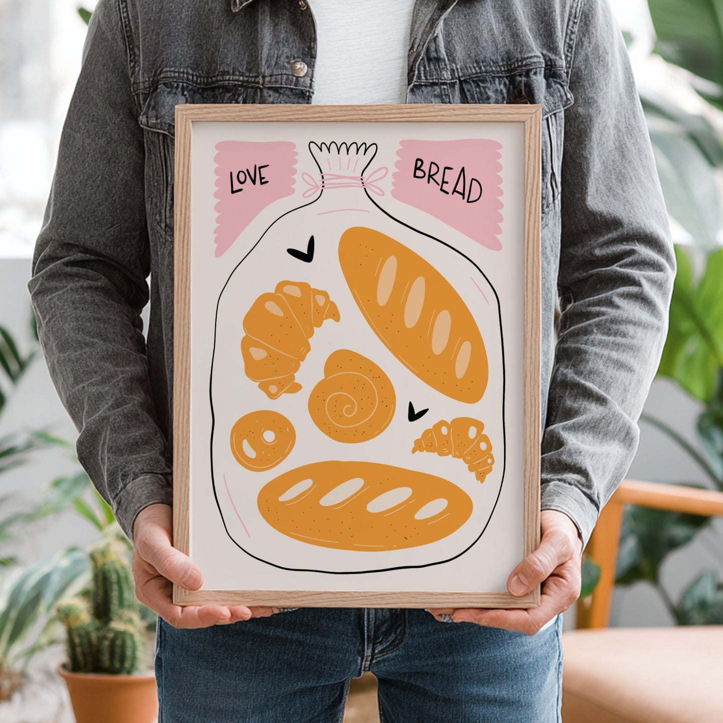 Person holding a framed illustration of bread with text 'Love Bread' in a casual setting.