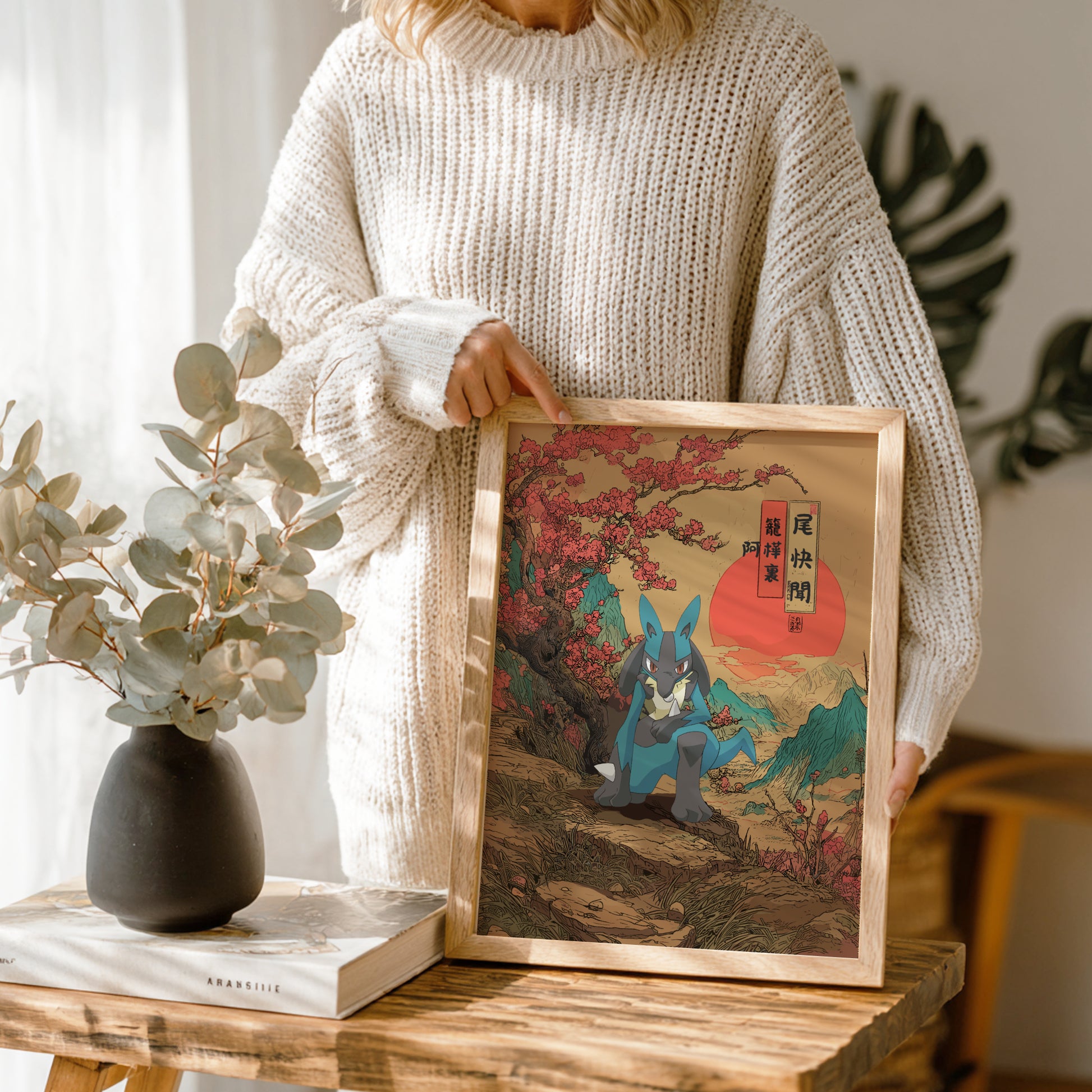 Person holding a framed artwork of Lucario Pokemon with cherry blossoms, wearing a beige sweater.