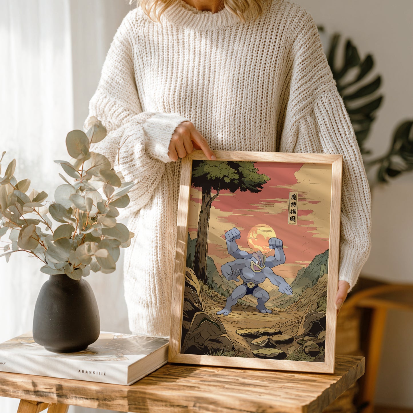 Person holding a framed artwork of a stylized Machamp Pokémon character in a natural setting