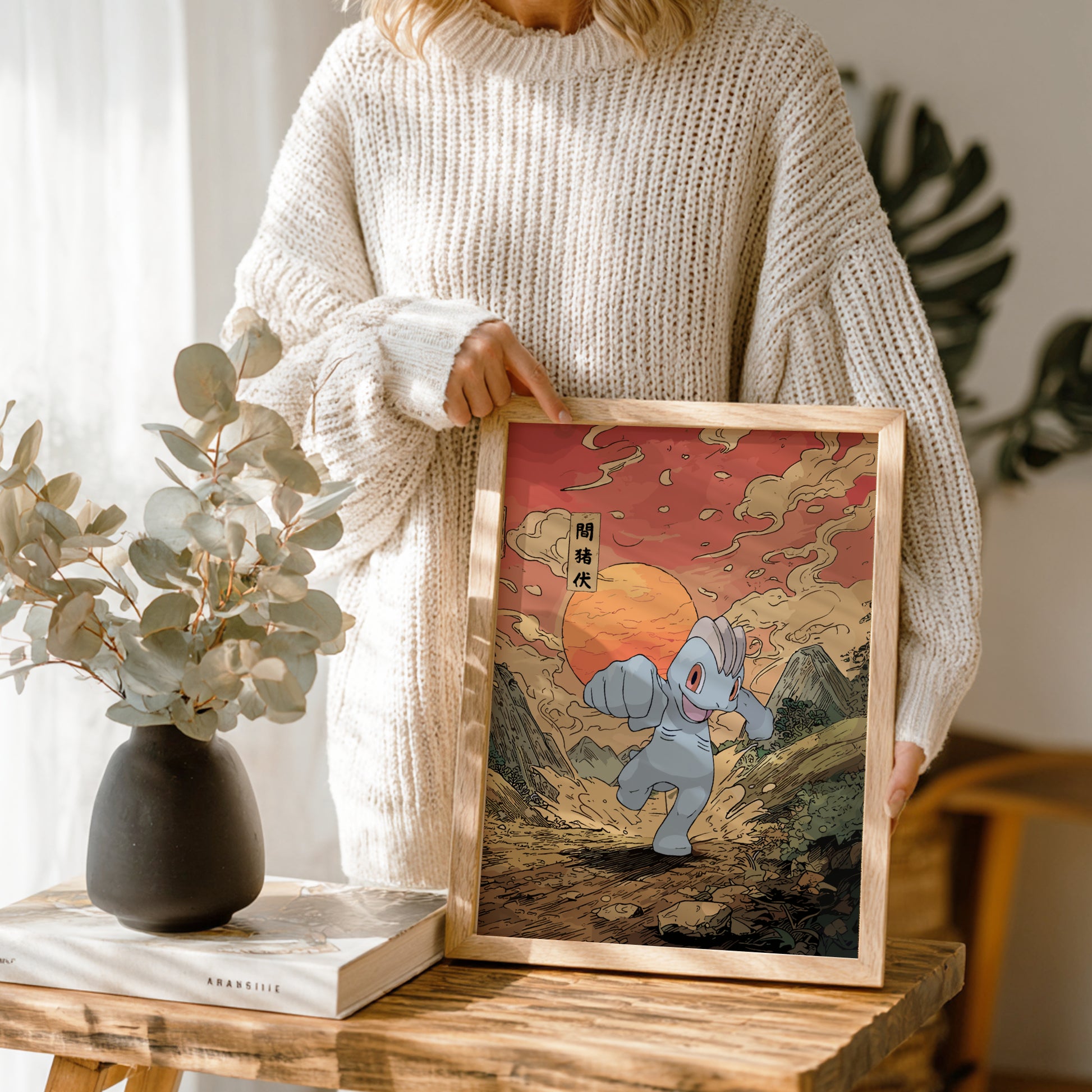 Person holding a framed artwork of Machop Pokemon character in a scenic setting