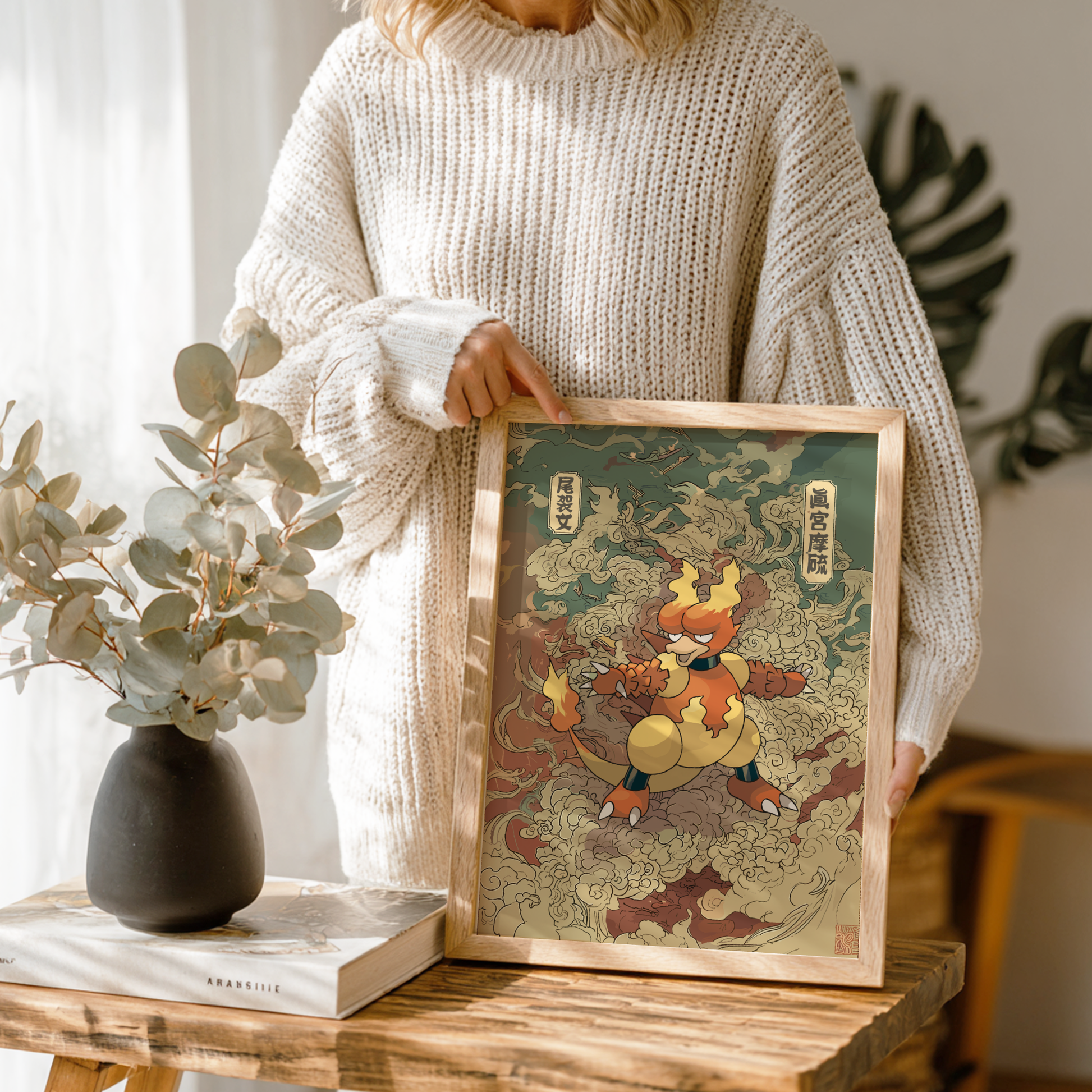 Person holding a framed artwork of Magmar Pokemon in a home setting