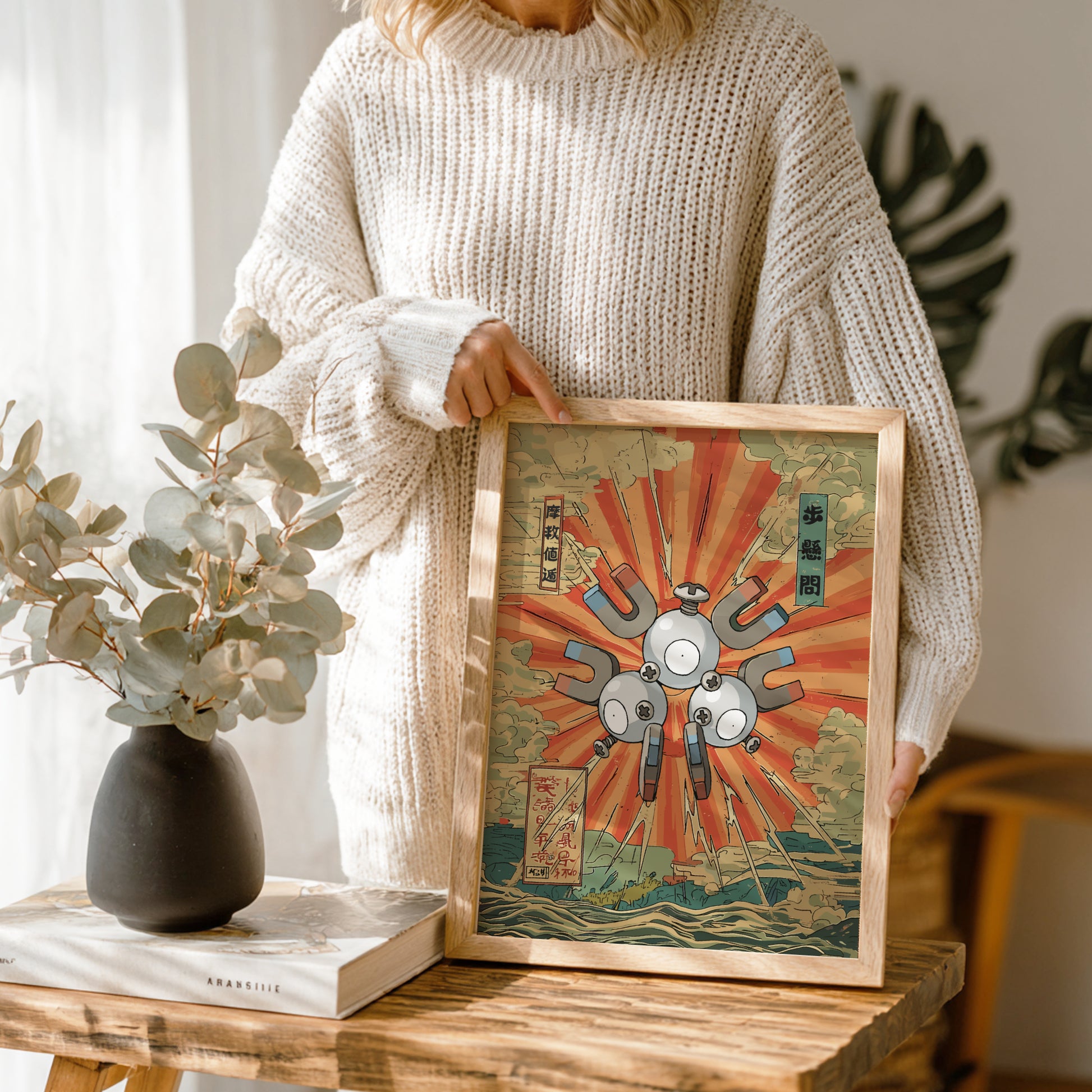 Person holding a framed artwork with a Magneton Pokemon and abstract design, standing in a room with plants and decor.