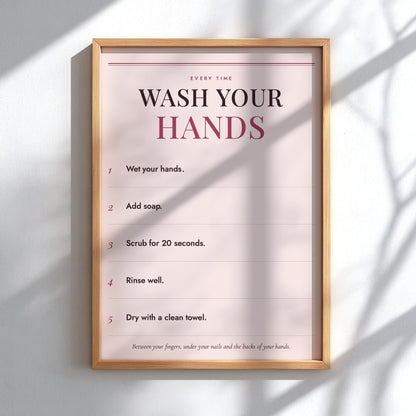 A framed handwashing instruction poster hanging on a white wall, with sunlight casting soft shadows across the print and frame.