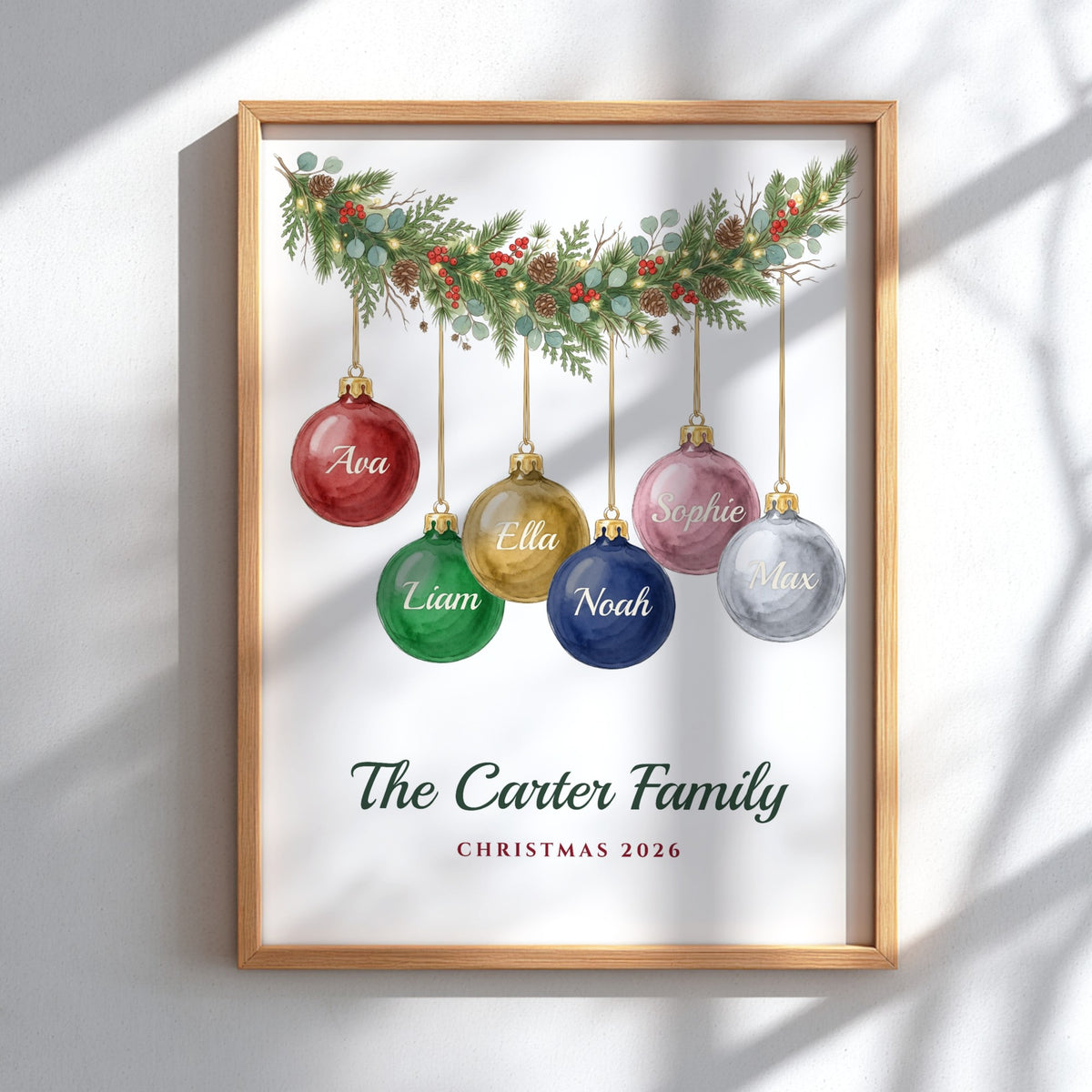 A personalized framed Christmas print featuring six hanging ornament illustrations in red, green, gold, pink, blue, and silver, with the text 'The Carter Family' and 'Christmas 2026' below. The print is shown in a light wood frame against a white wall with soft shadow overlays.