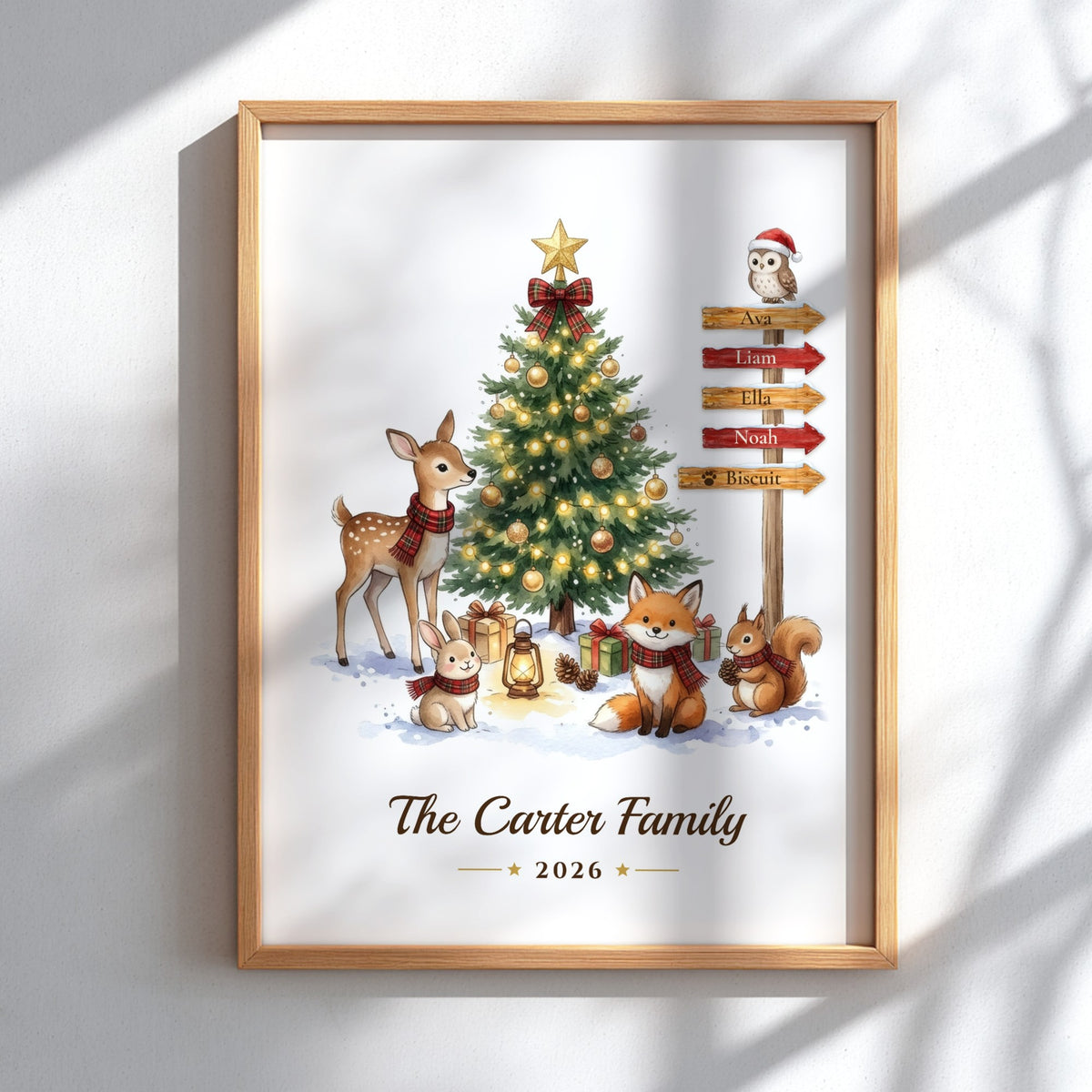 A personalized framed Christmas art print featuring cartoon deer, fox, squirrel, and an owl around a decorated tree, with a wooden signpost and the text 'The Carter Family 2026'. The print is shown hanging on a white wall with soft window shadows.