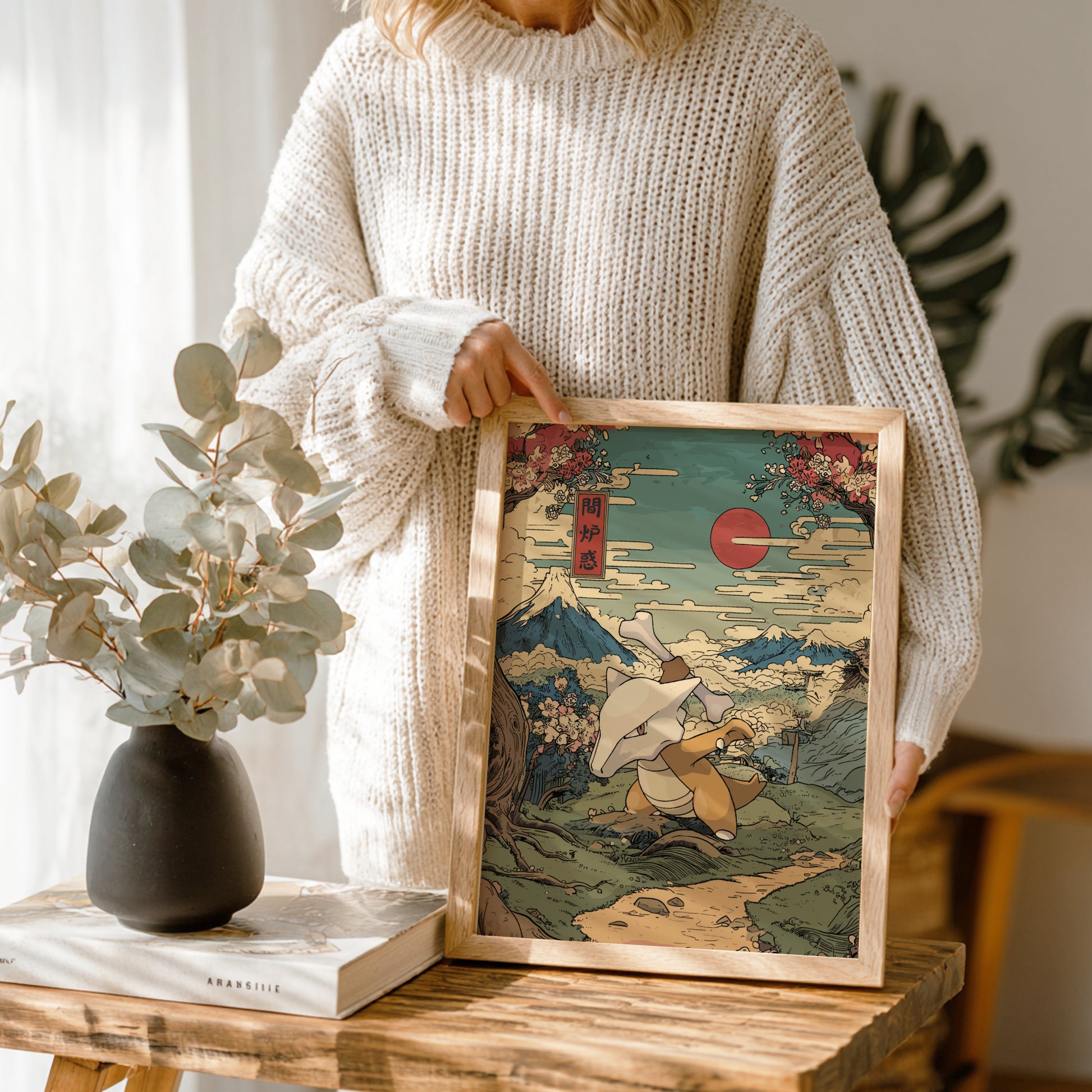 Person holding a framed artwork of a traditional Japanese scene with Mount Fuji and Marowak Pokemon.