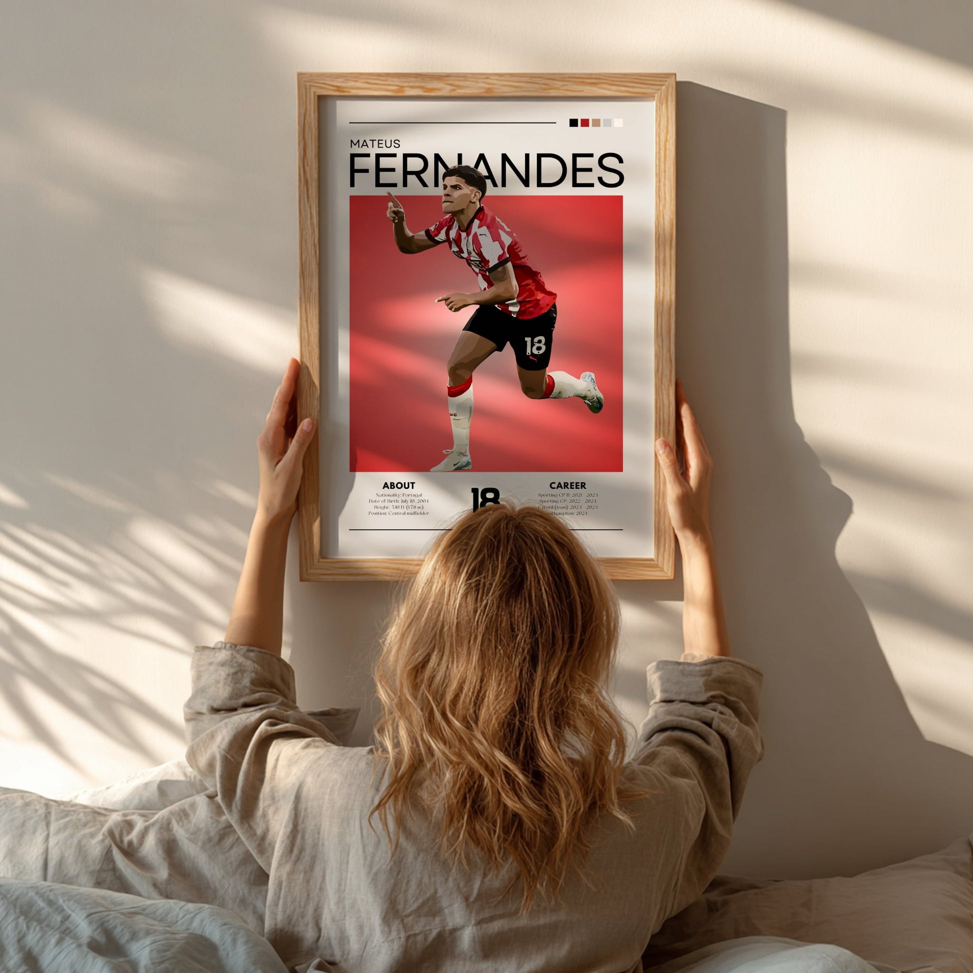 Person hanging a framed poster of a soccer player named Fernandes on a wall.