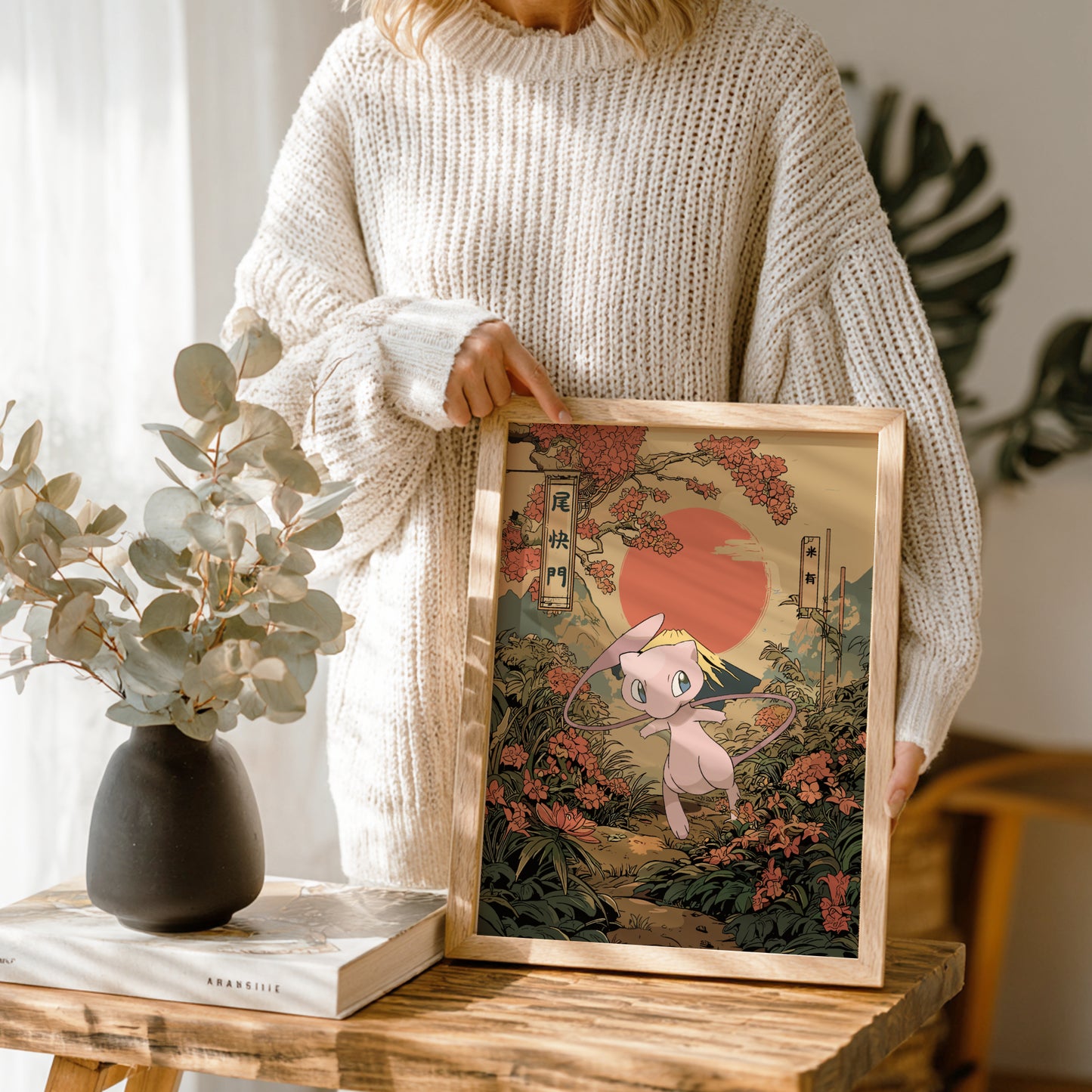 Person holding a framed artwork of Mew Pokemon character in a scenic setting