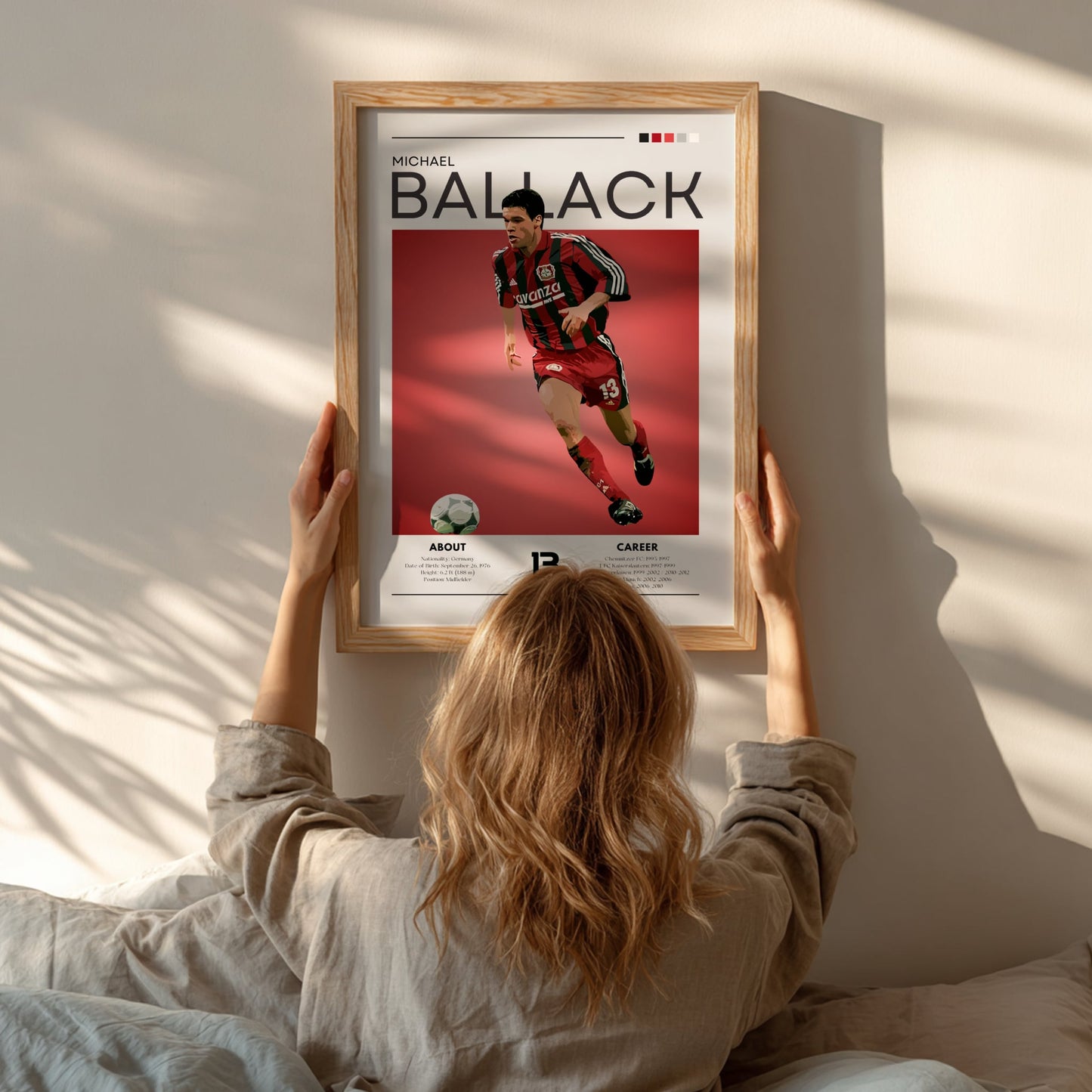 Person hanging a framed poster of Michael Ballack on a wall