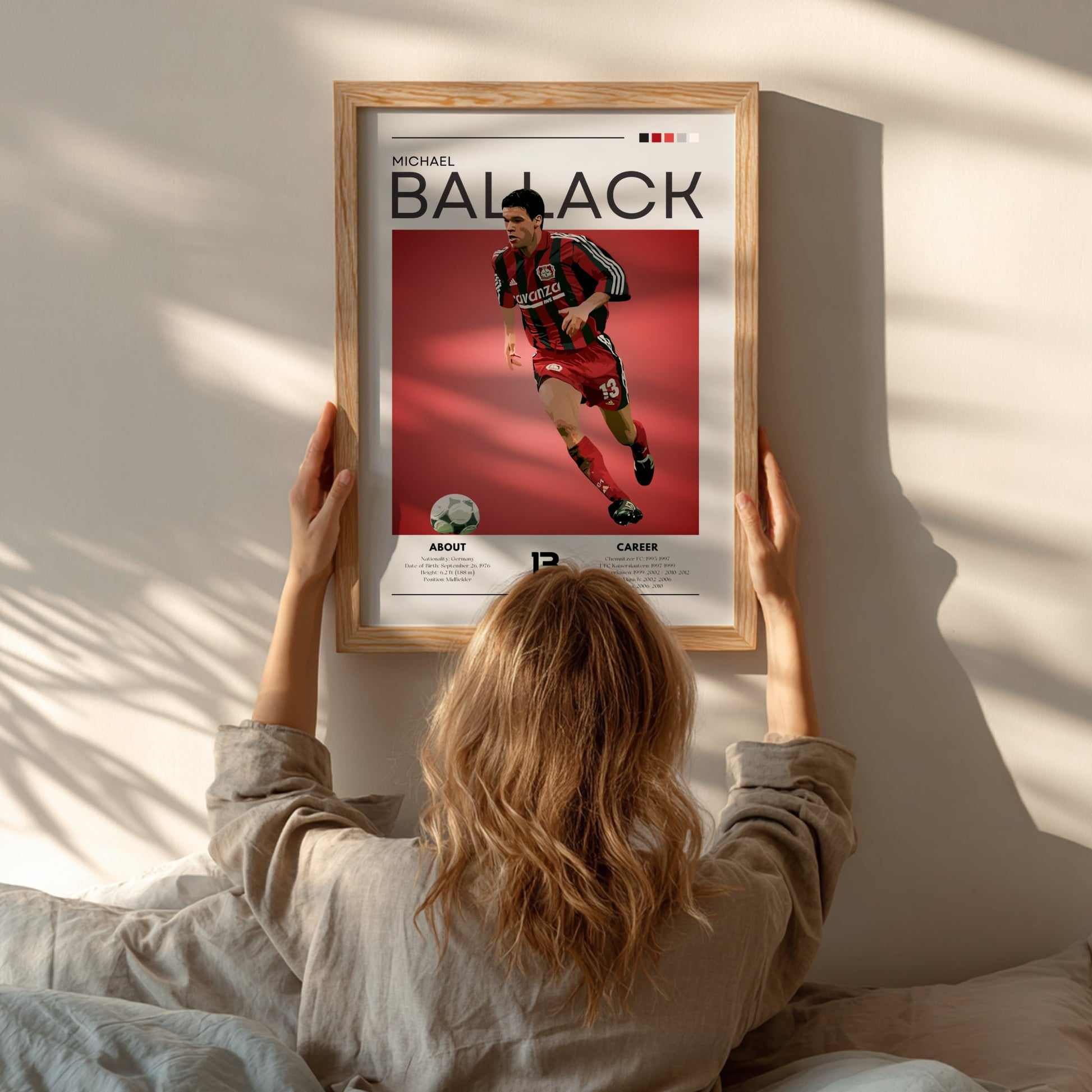 Person hanging a framed poster of Michael Ballack on a wall