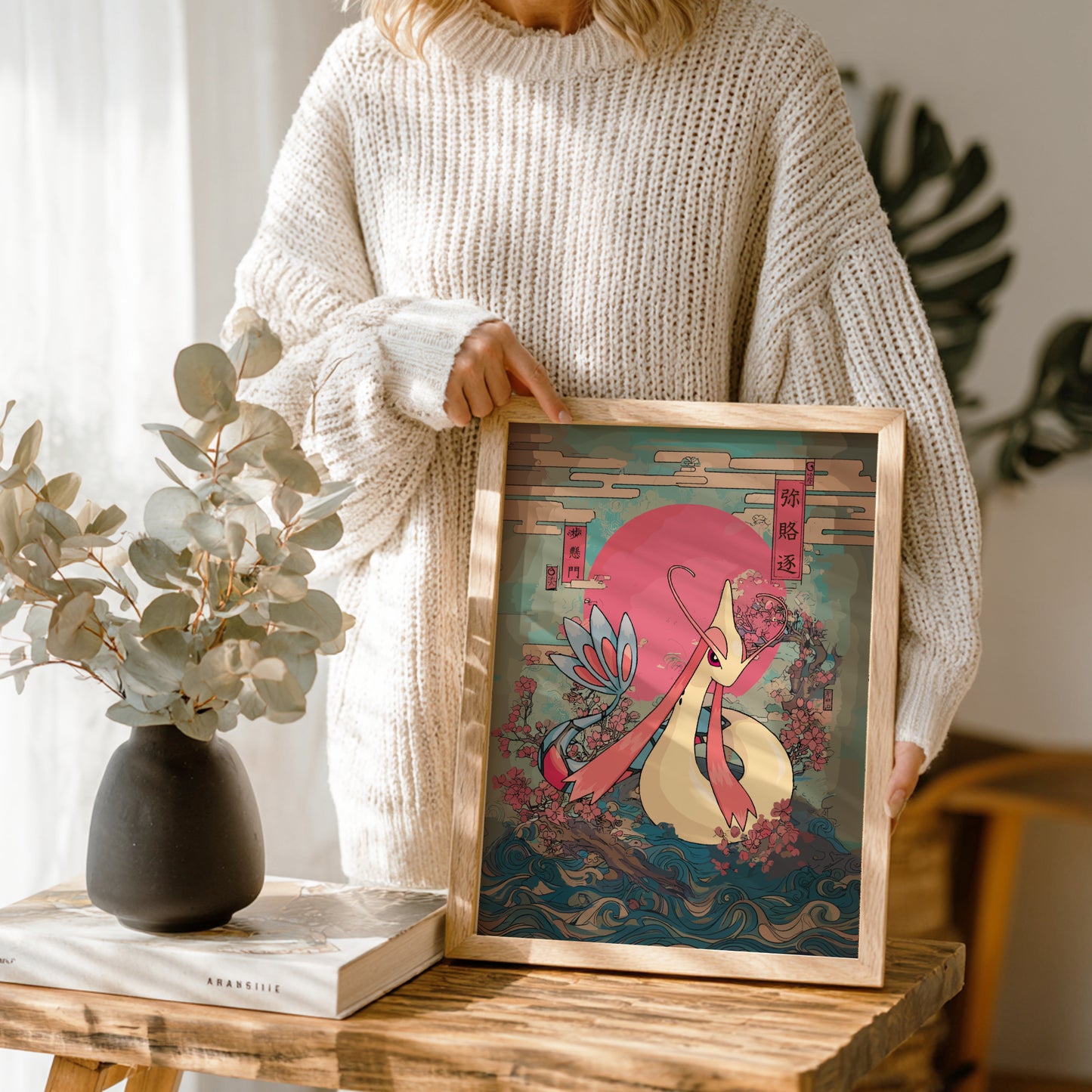Person holding a framed artwork with Milotic Pokemon design in a home setting.