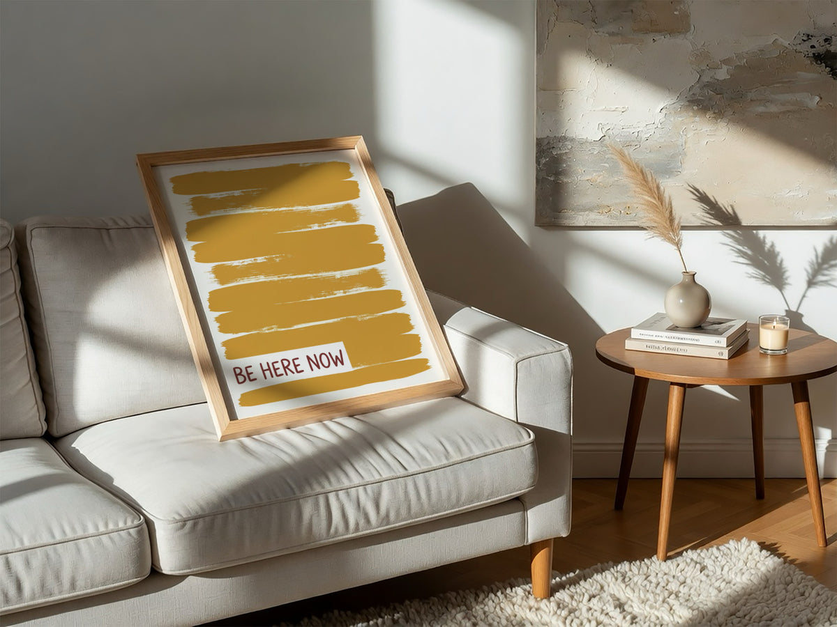 Motivational poster with yellow brushstrokes and the text Be Here Now in brown